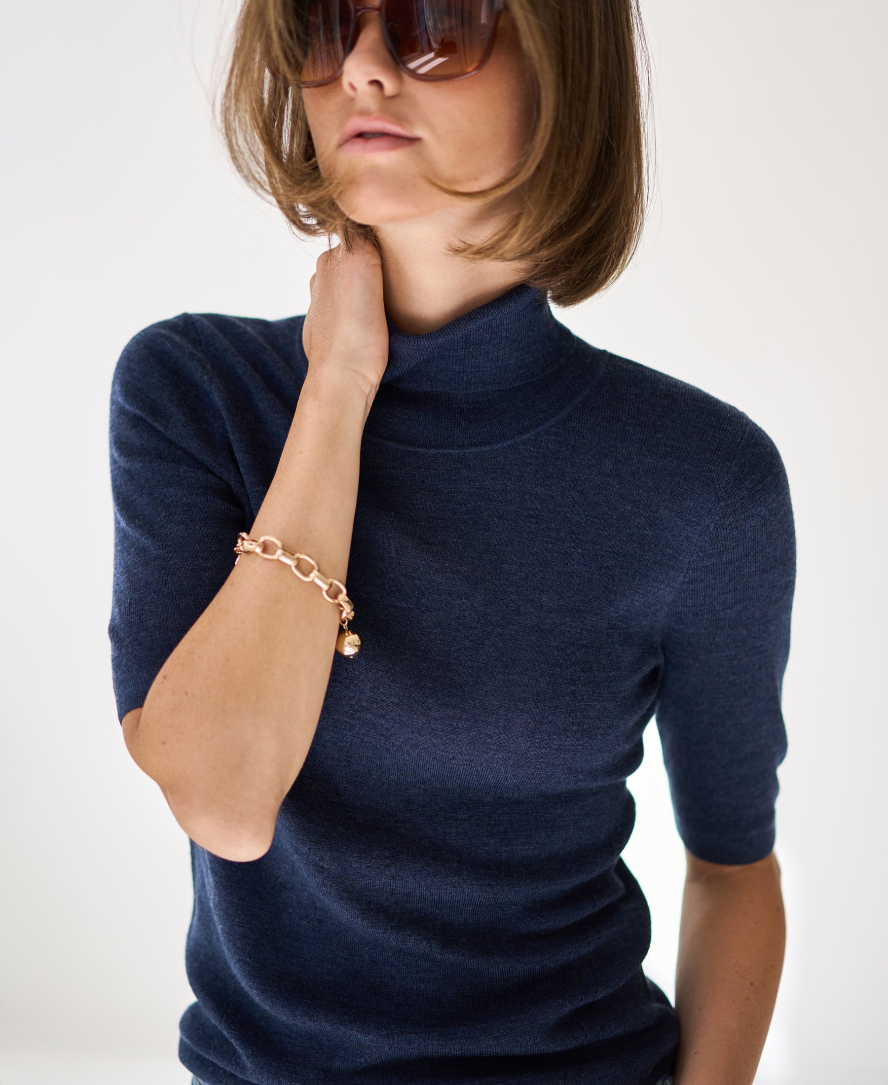 Woman wearing a short sleeve turtleneck sweater in blue, on a white background.