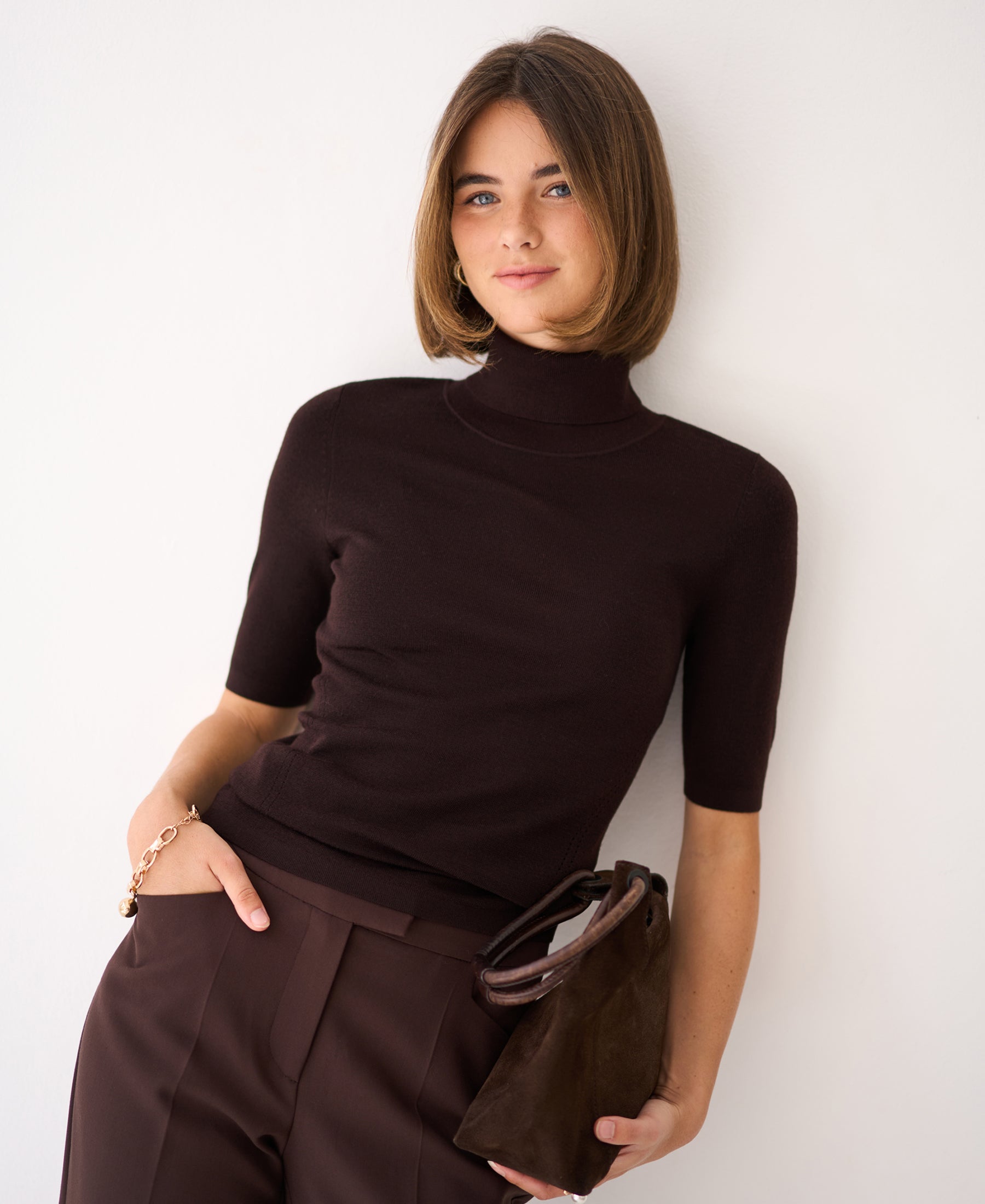 Woman wearing a short-sleeve turtleneck sweater in Pure Choco brown.