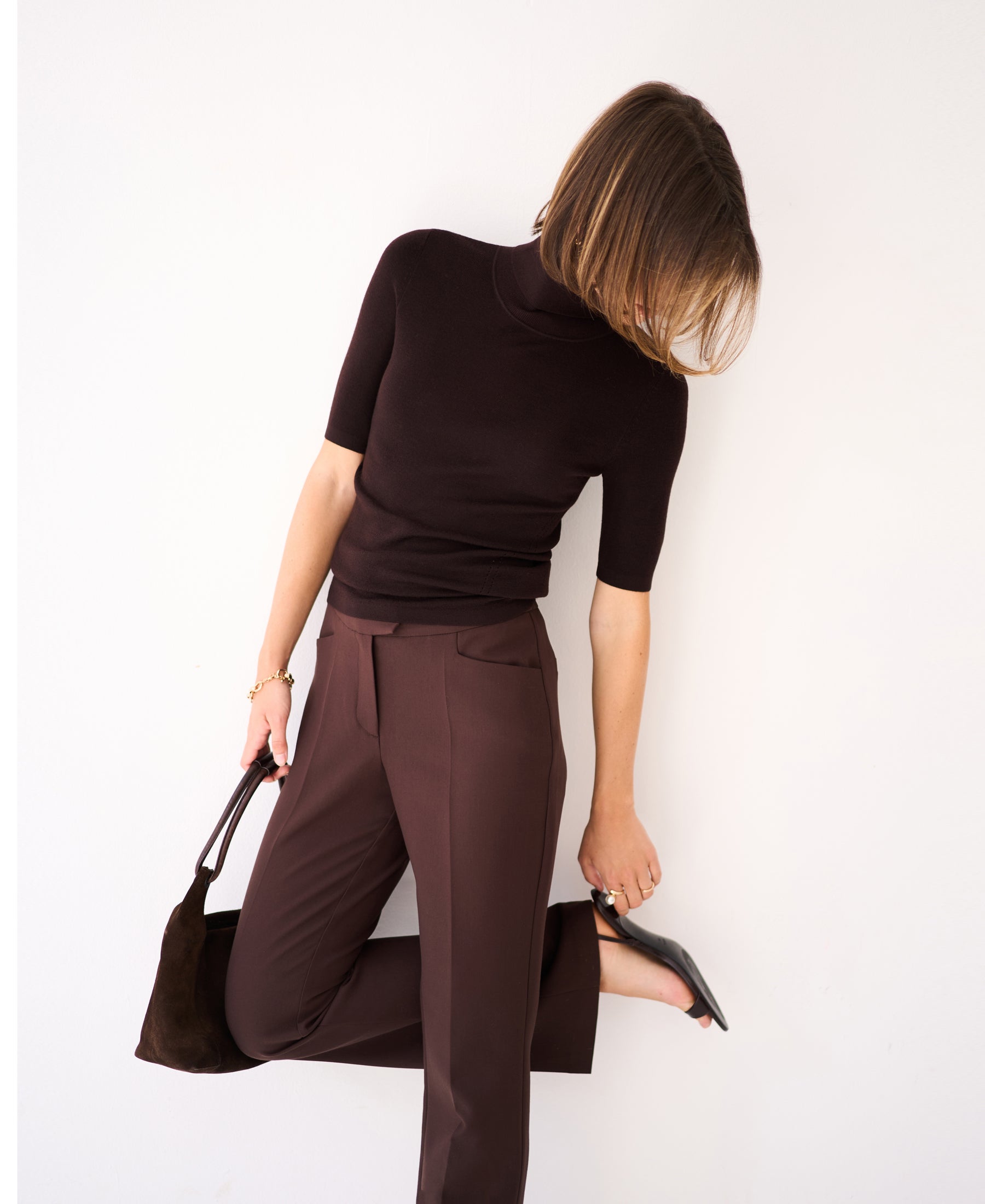Woman wearing short sleeve turtleneck sweater in pure chocolate brown, head tilted down.