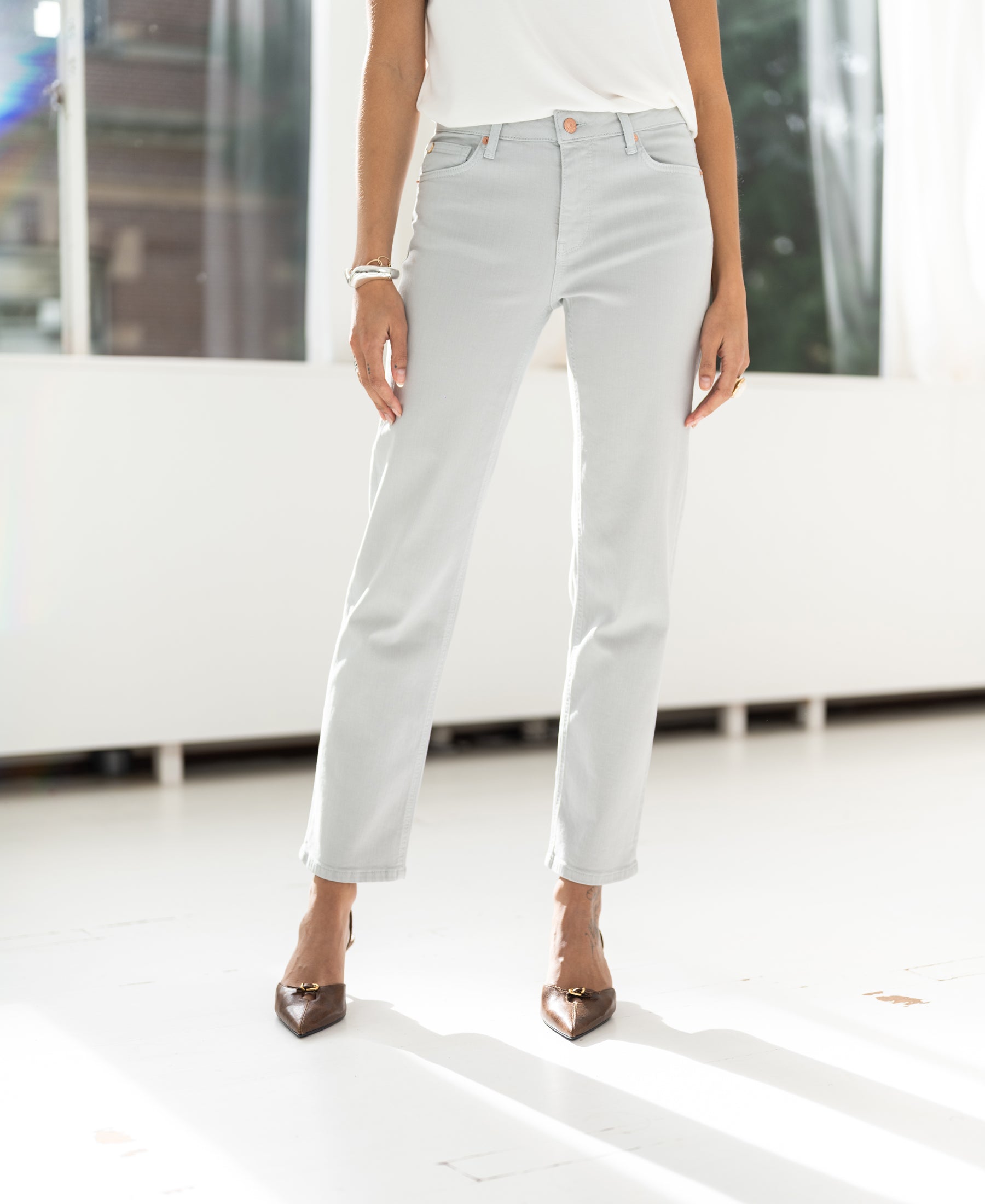 A woman wears light grey cropped jeans from PLEIN PUBLIQUE indoors.