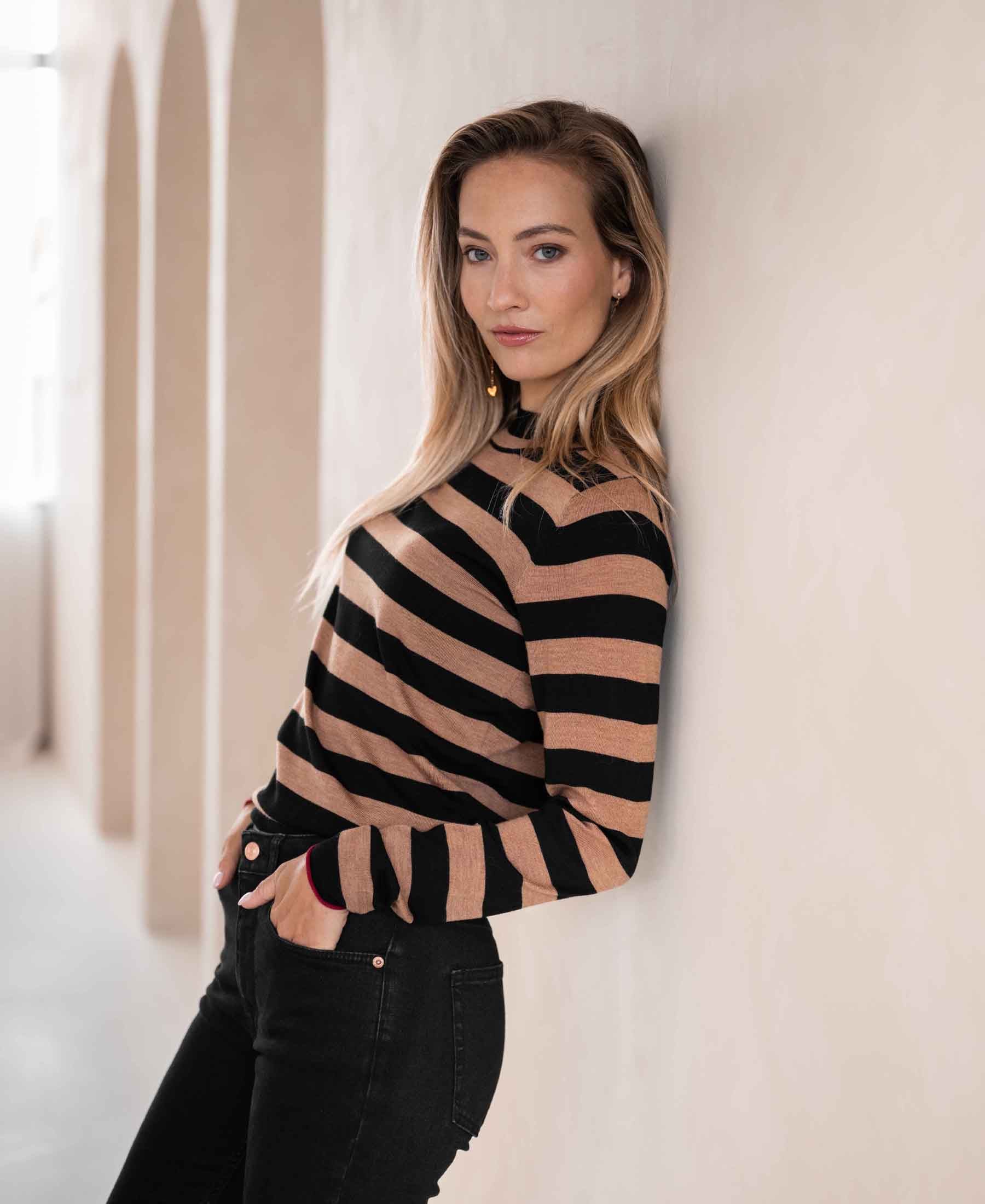 Black and beige striped turtleneck sweater, shown on a person leaning against a light wall.