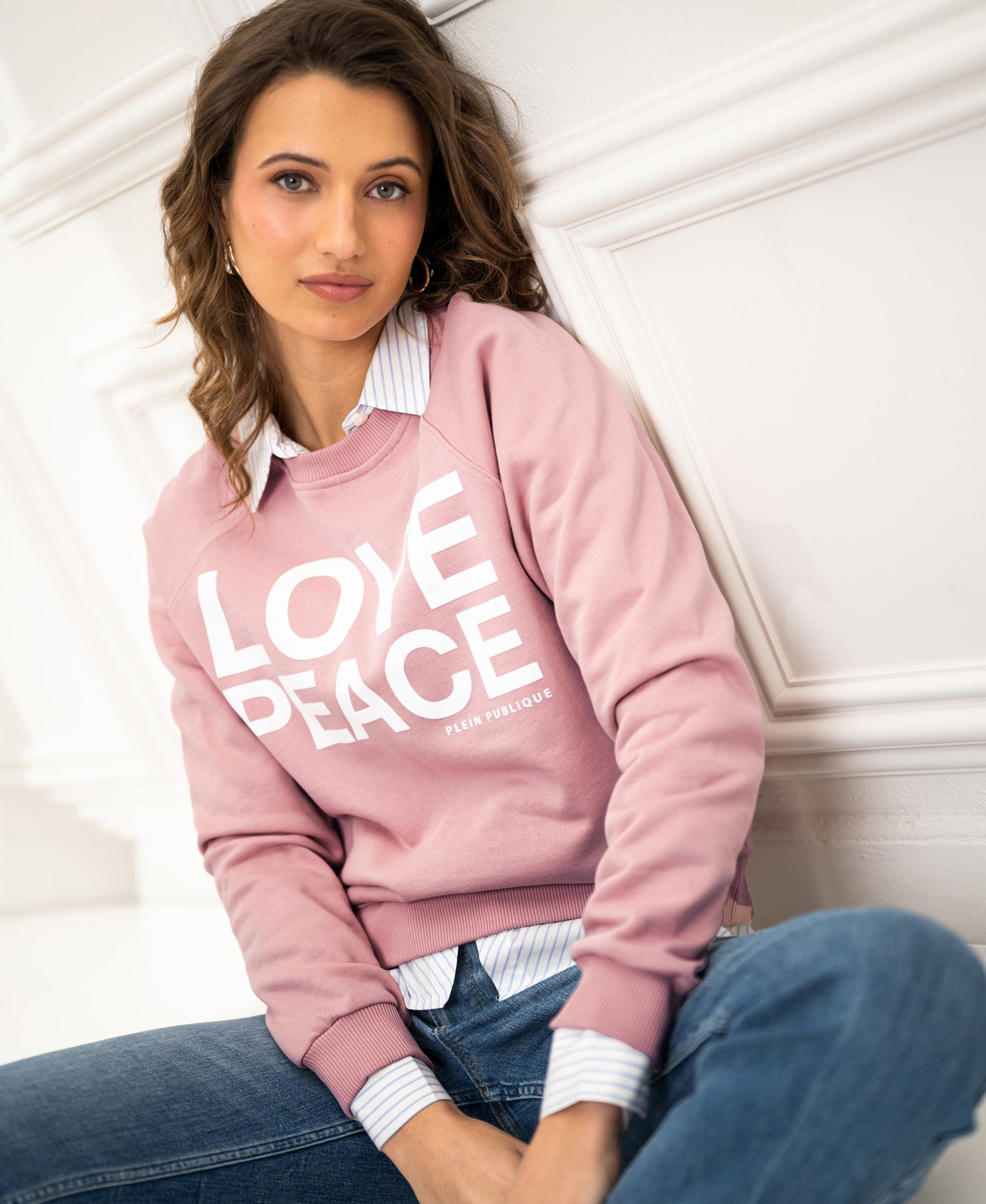 Antique rose LOVE PEACE sweater by Plein Publique, front view against a white paneled wall.