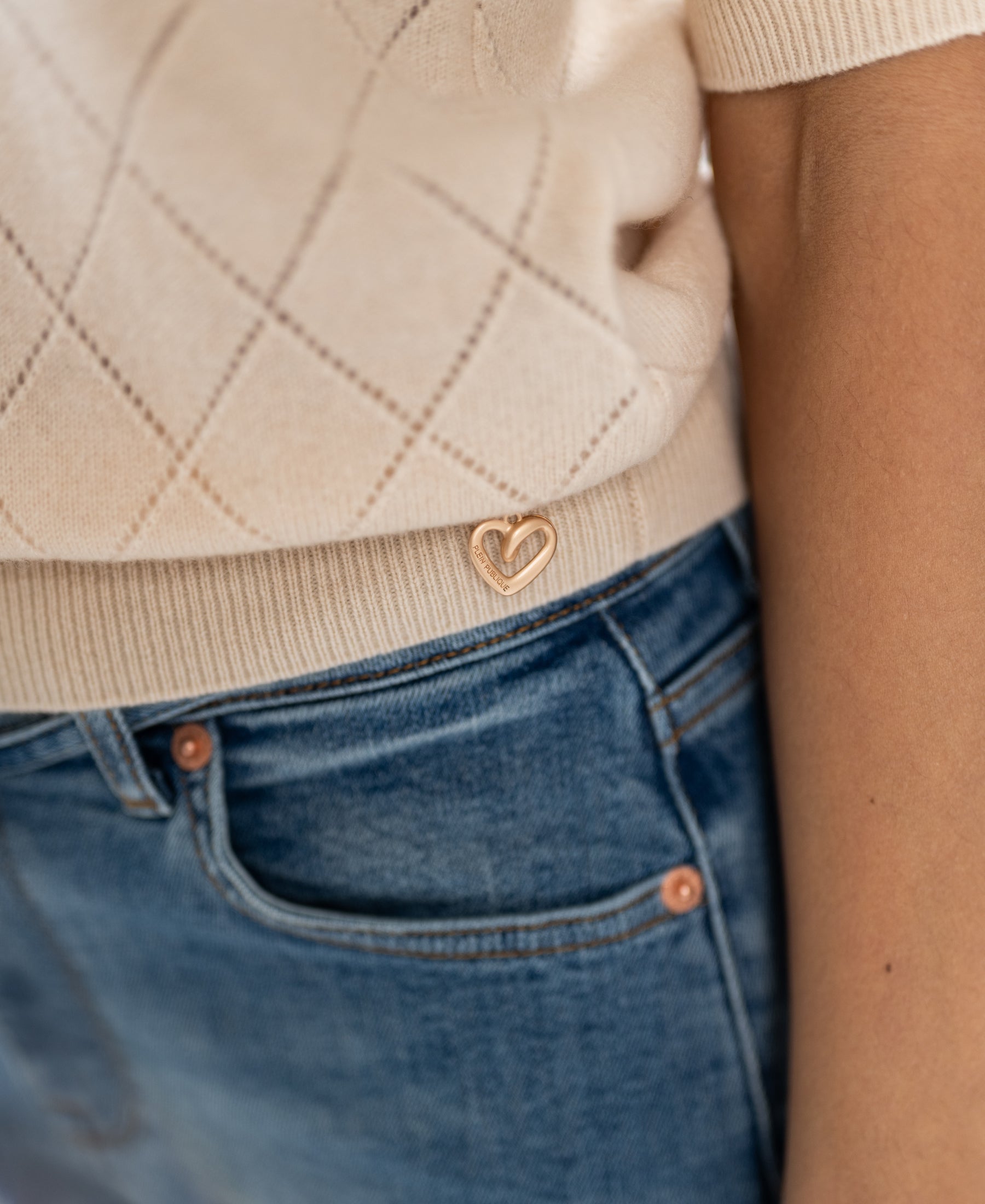 Argyle merino sweater in butter color with a gold heart pin near the hem.