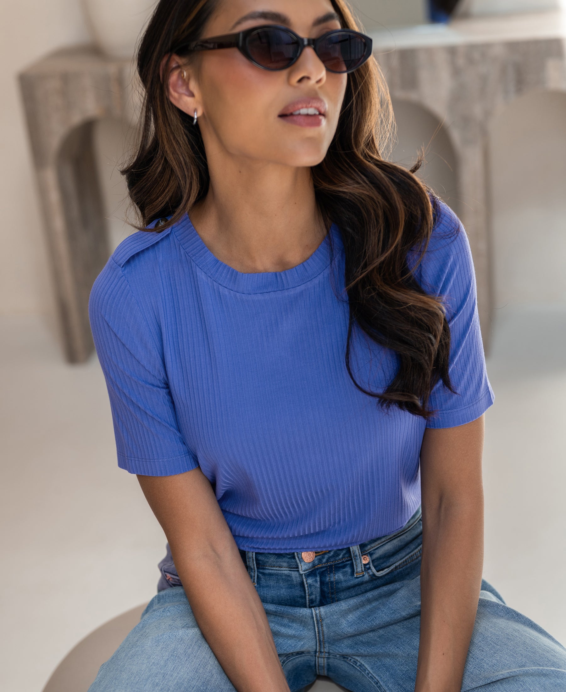 Woman wearing a bamboo T-shirt in lavender by PLEIN PUBLIQUE, seated indoors.