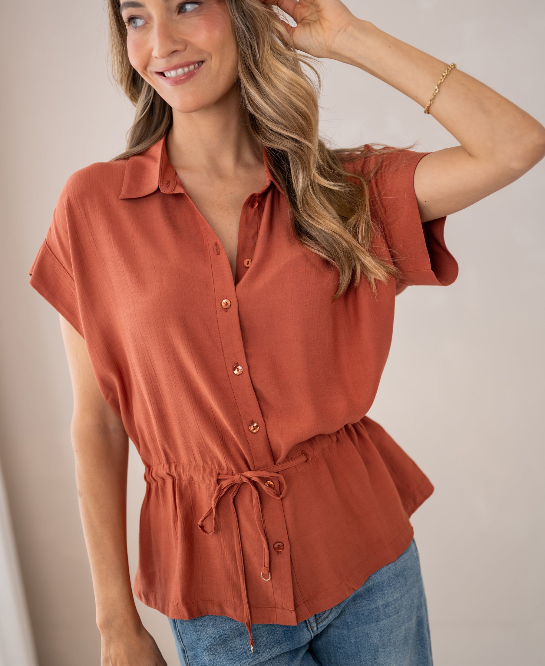 Woman wears a terra-colored viscose blouse by PLEIN PUBLIQUE, called LA JODY.