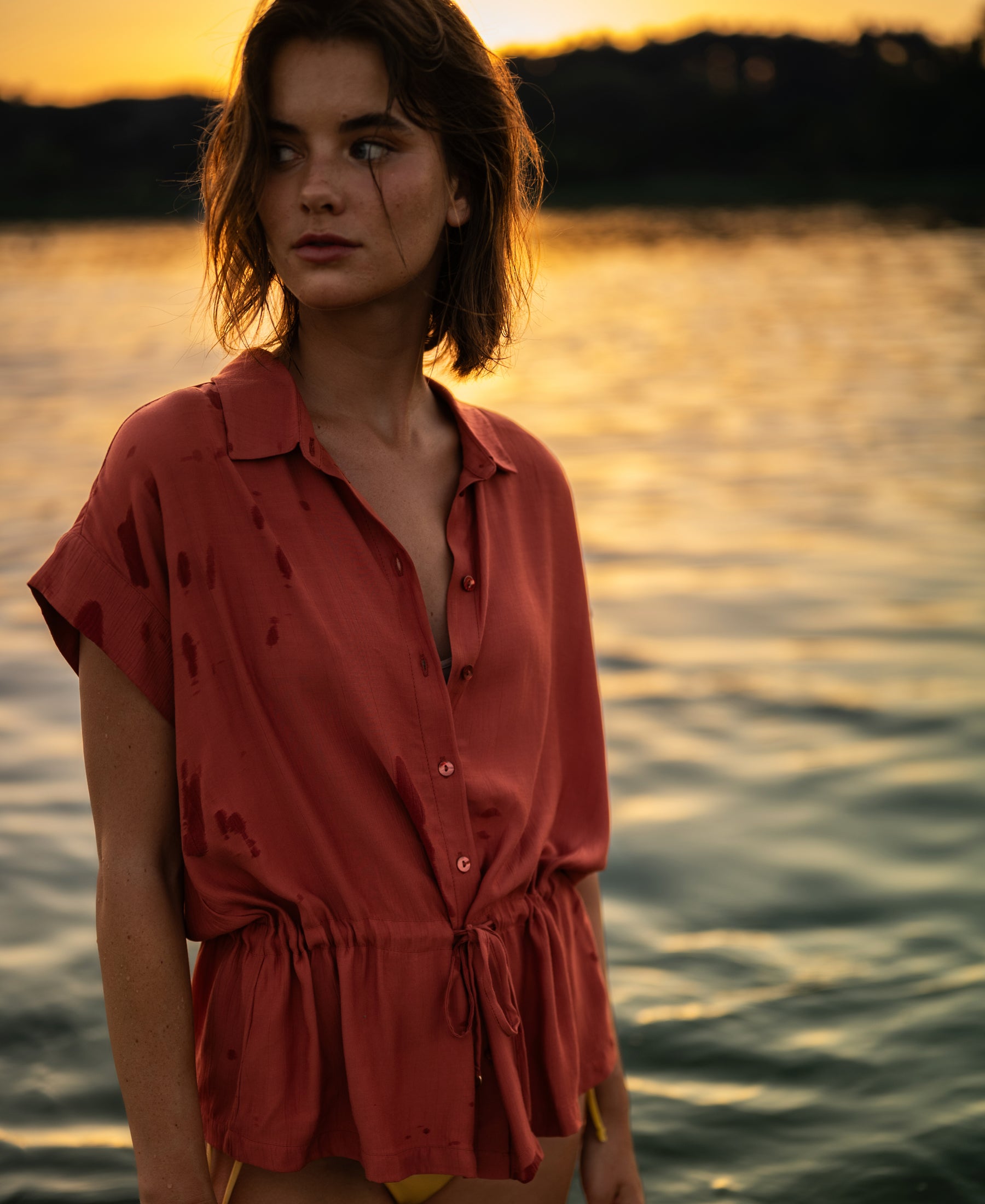 A woman wears a terra-colored LA JODY blouse by PLEIN PUBLIQUE with soft sunset light highlighting the shirt.