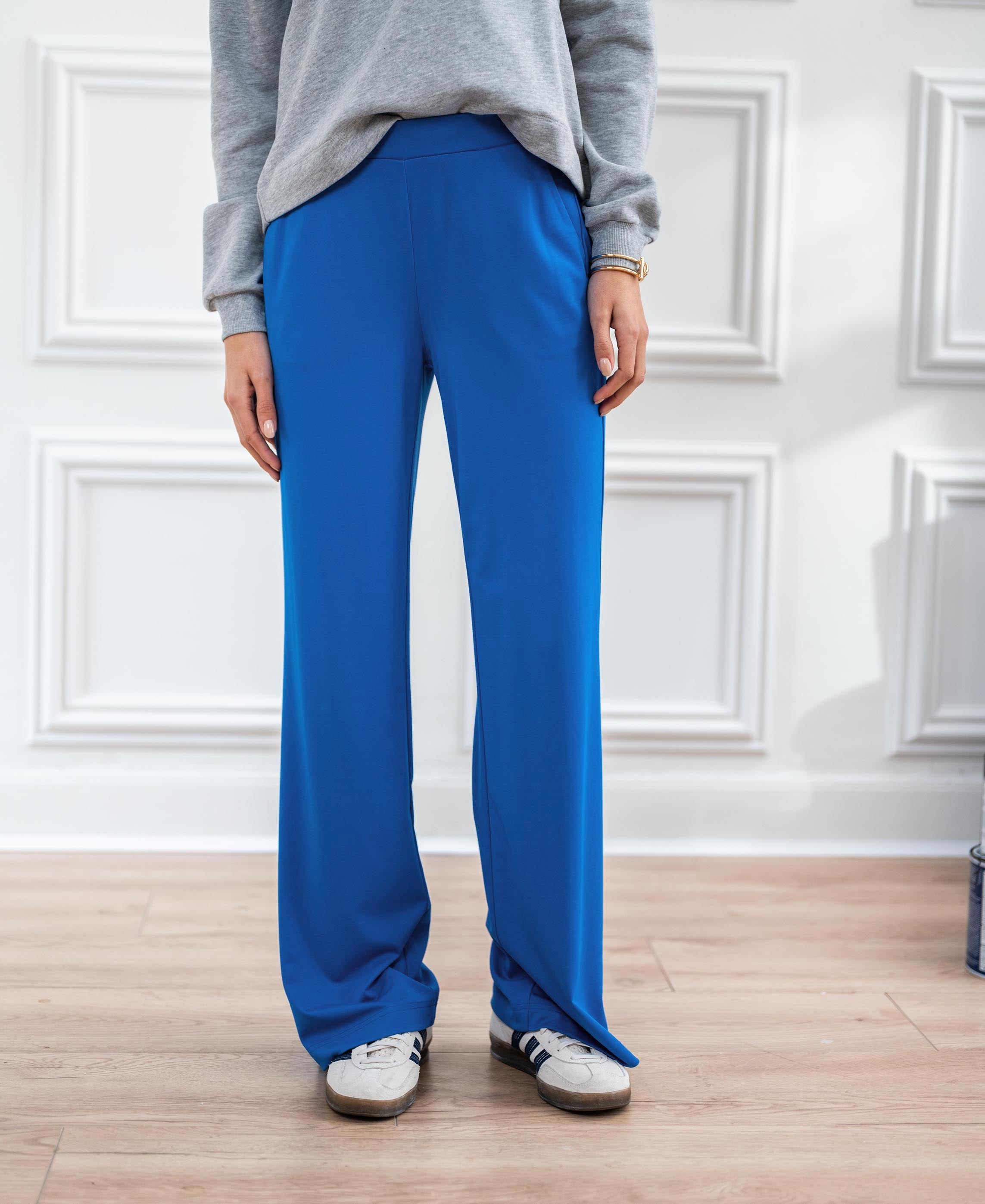 Blue LES JULES travel pants shown on a person, standing on a light wood floor.