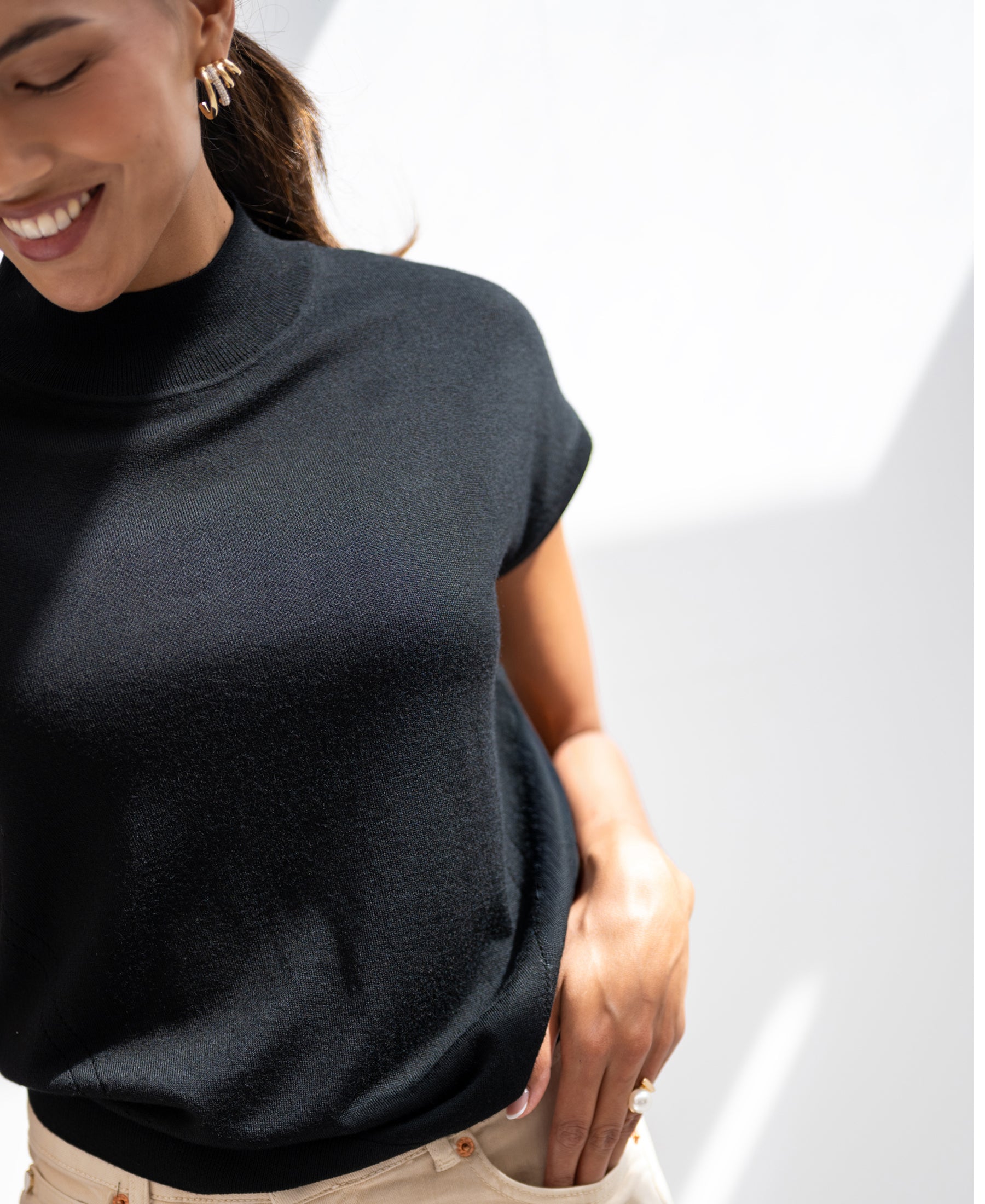 Woman wears black Merino wool top in sunlight, hand on hip.