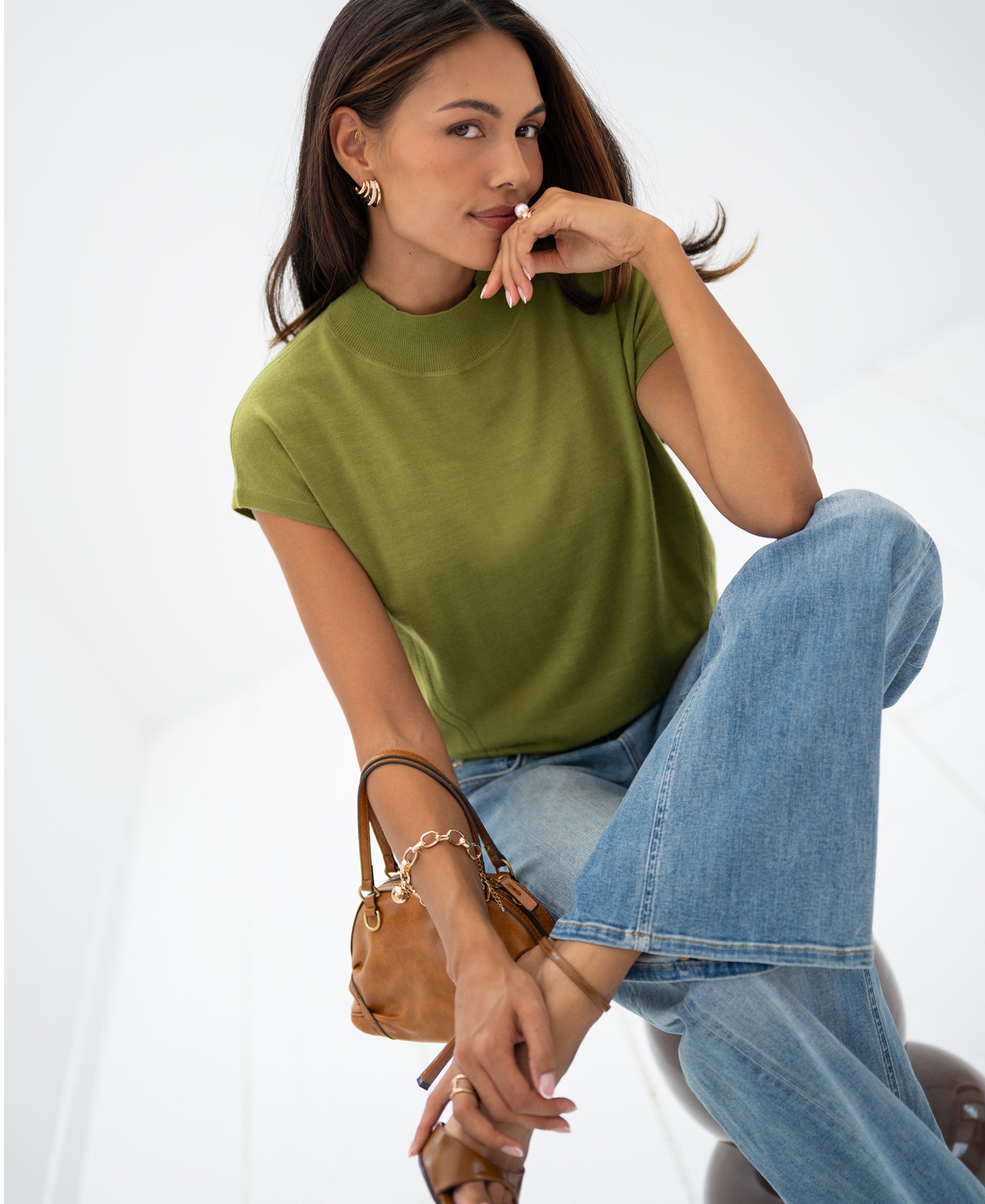 Woman wearing an olive green Merino wool top sits in a bright room.