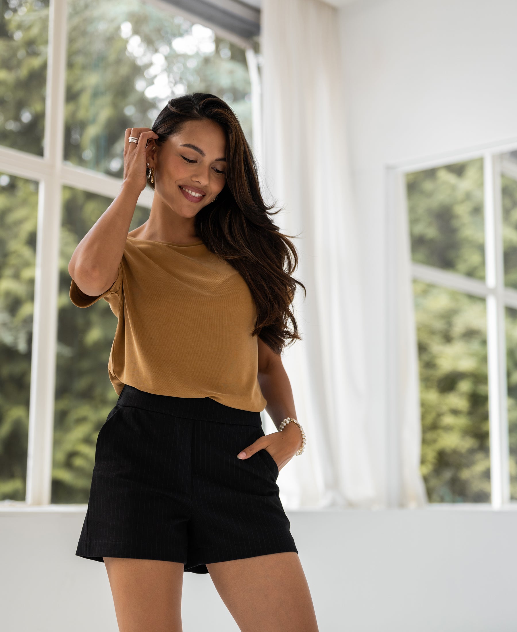 Light camel T-shirt in soft jersey fabric, shown on a model standing indoors.