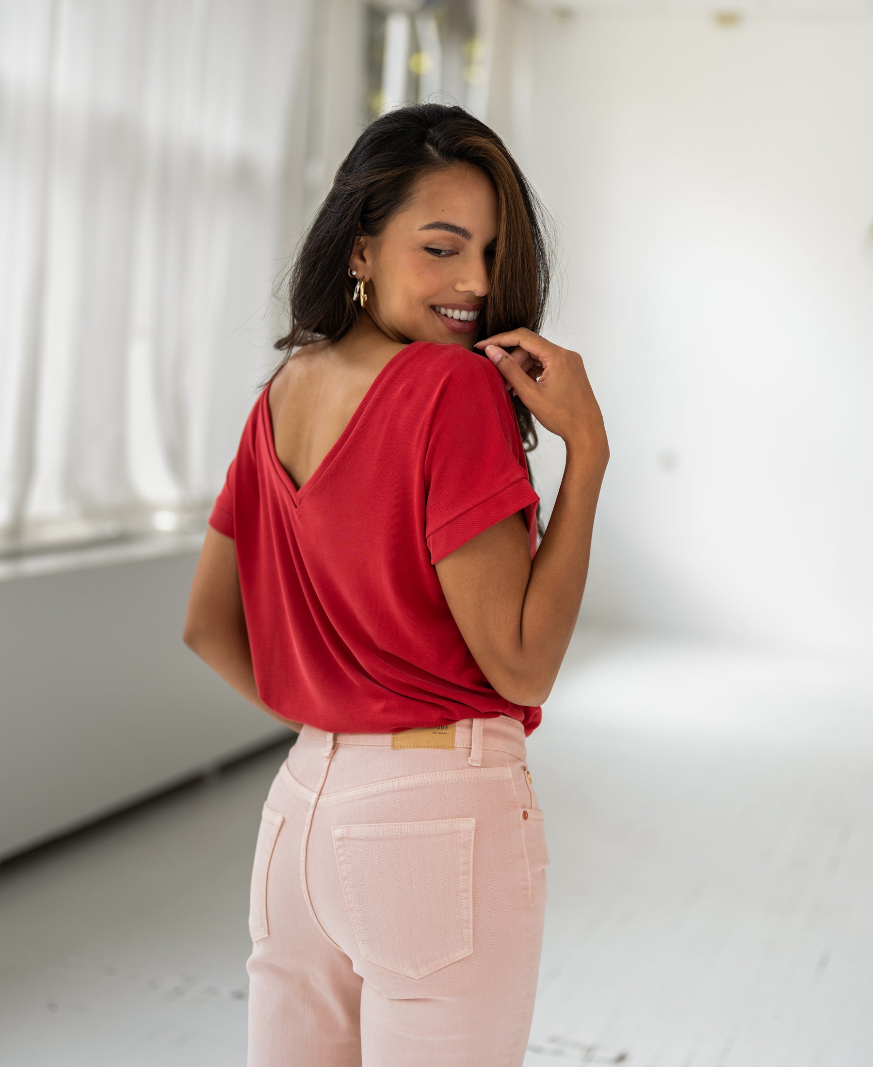 Woman smiles over her shoulder wearing the PLEIN PUBLIQUE Two-way T-shirt in red.