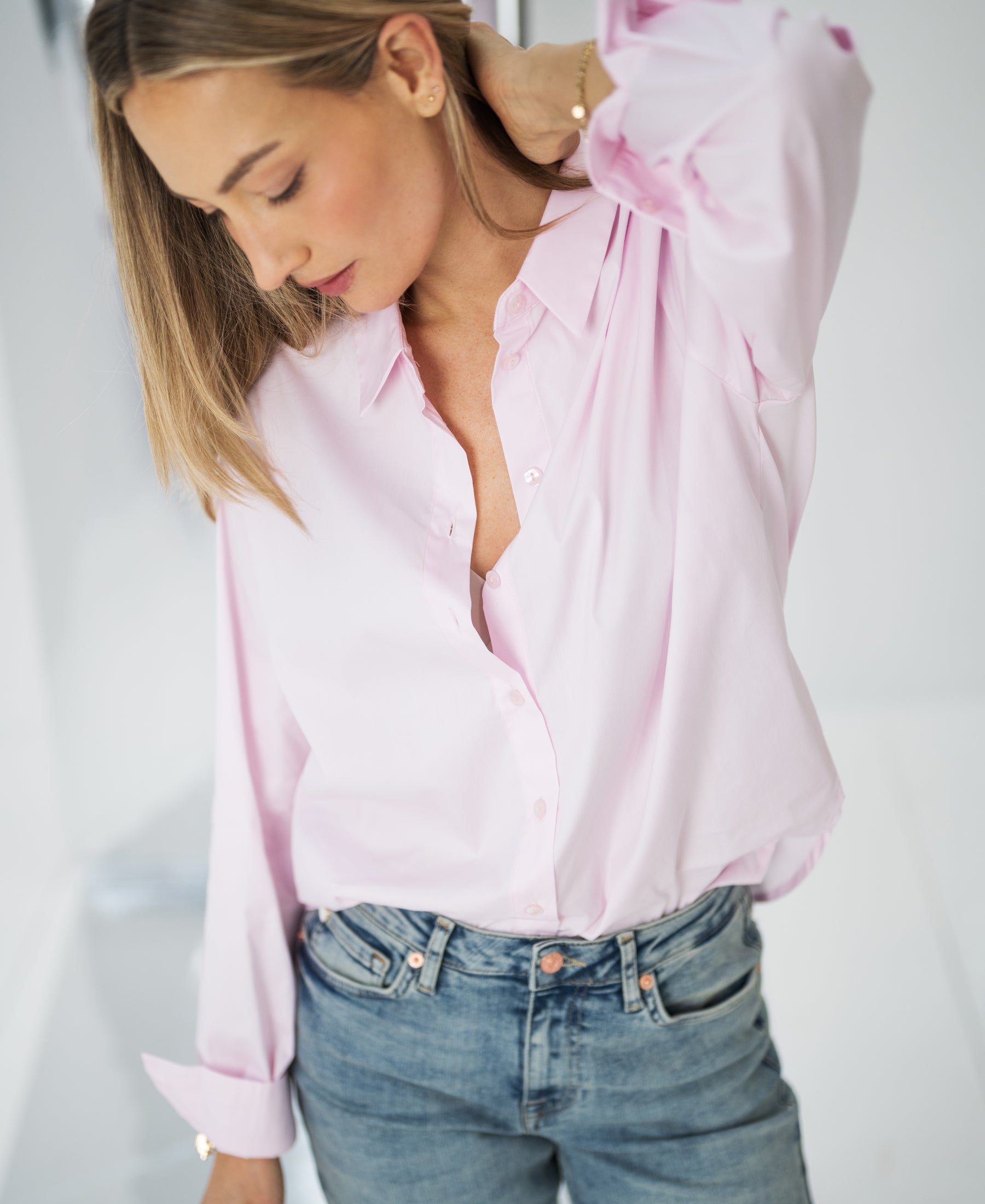 Oversized blouse LE LILLE in light pink, worn by a woman with blonde hair, looking down and touching her hair.