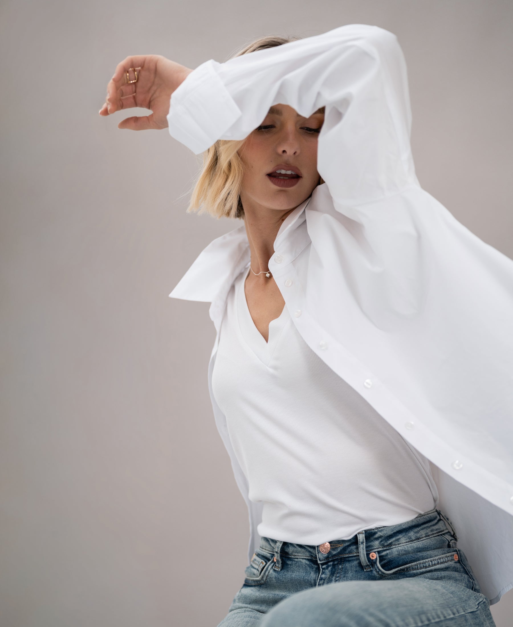 Woman wearing a white lyocell top poses with one arm raised, partially covering her face.