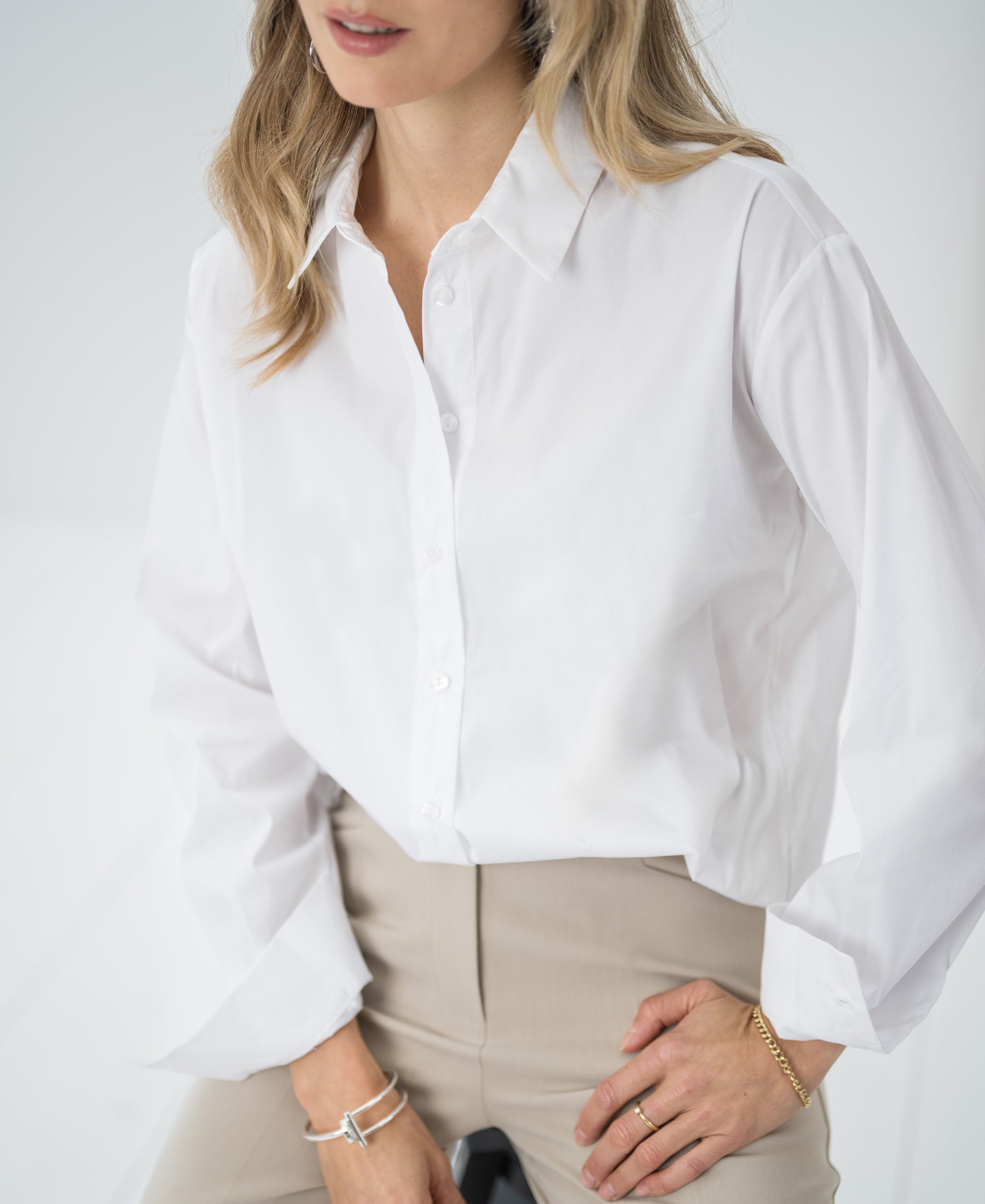 Woman wearing oversized white "LE LILLE" blouse, seated with one hand on her hip.
