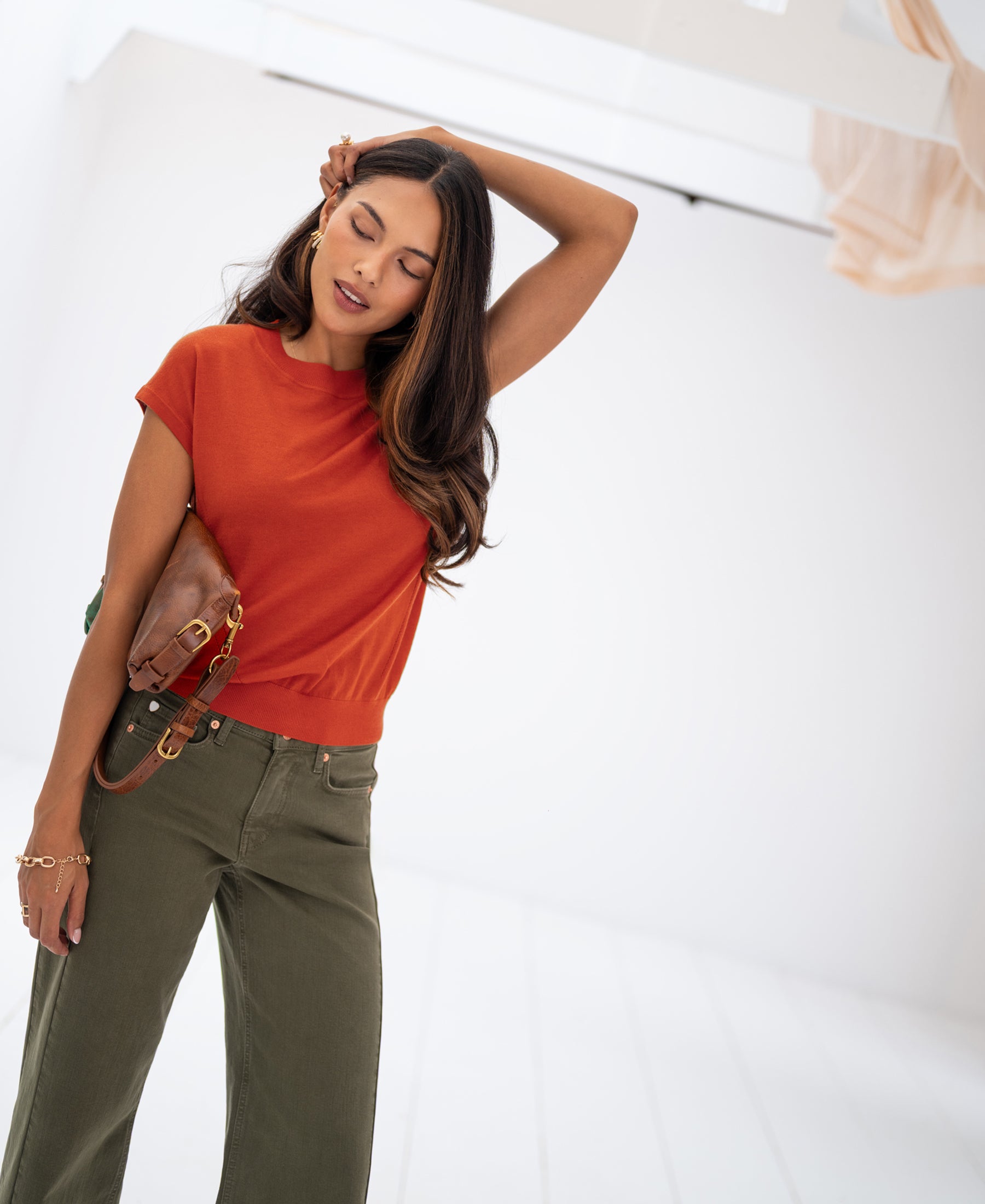 Woman wears the Merino Wool Top in chili, posing in a bright room.