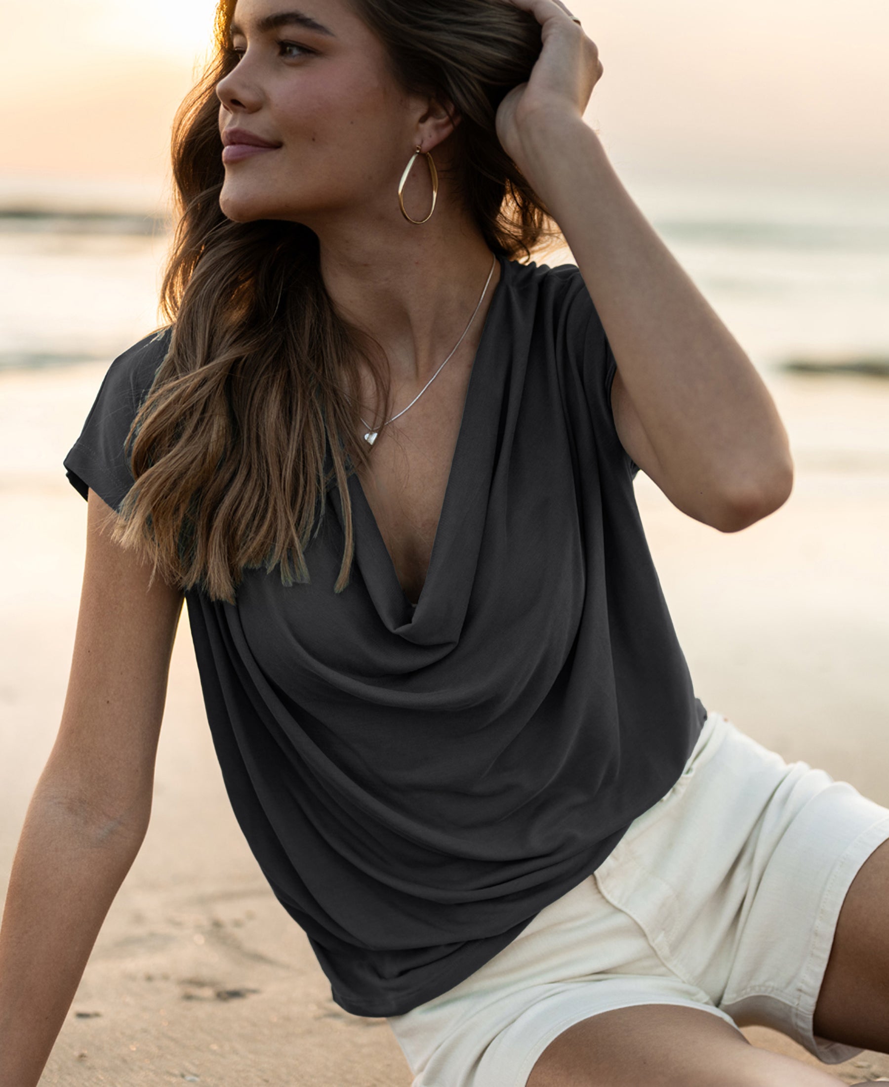 Woman wearing a charcoal draped-neck top from PLEIN PUBLIQUE LA LUCA collection at sunset.