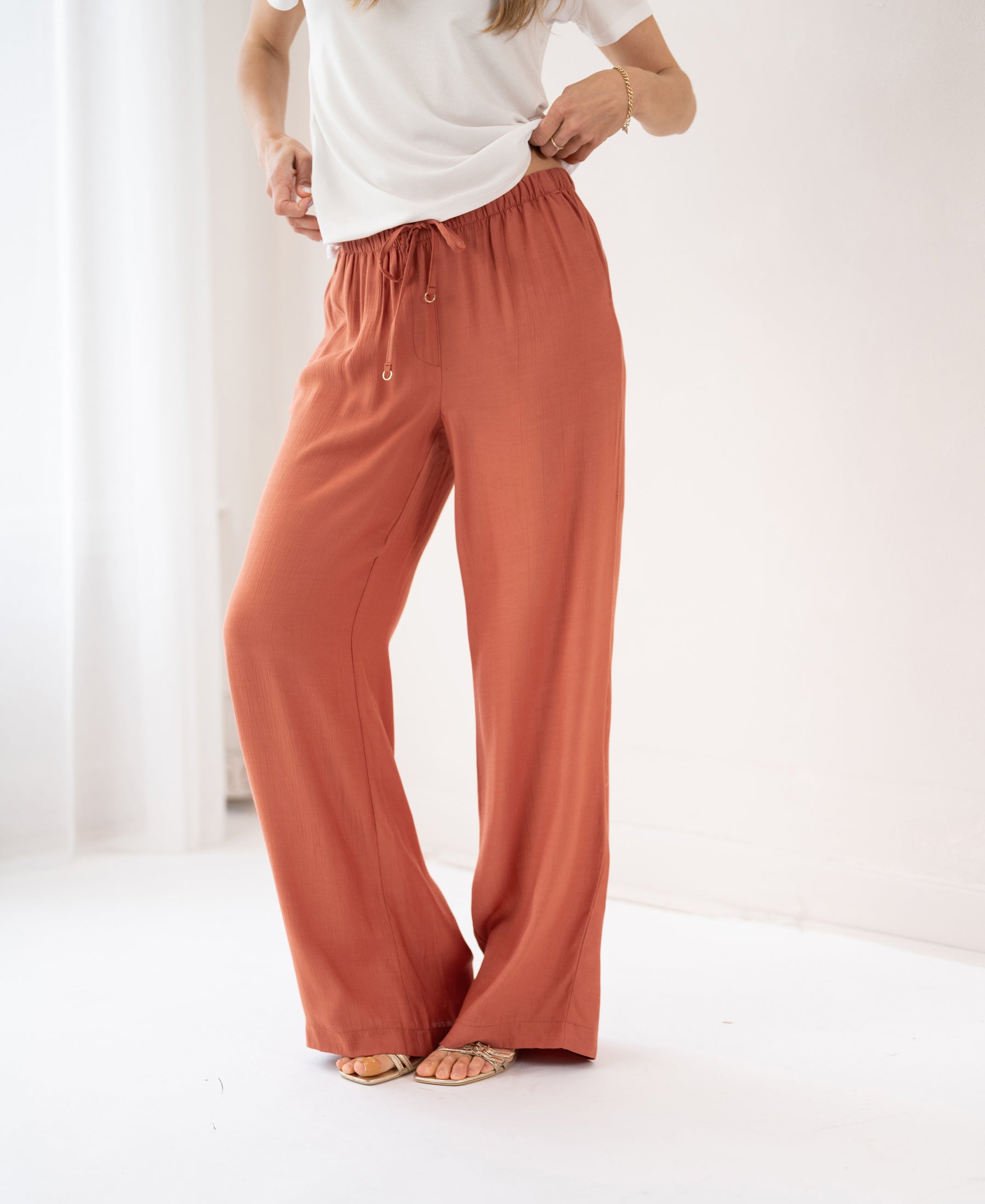 Rust wide leg pants, product name LA LYNETTE Terra by PLEIN PUBLIQUE, shown on white floor.