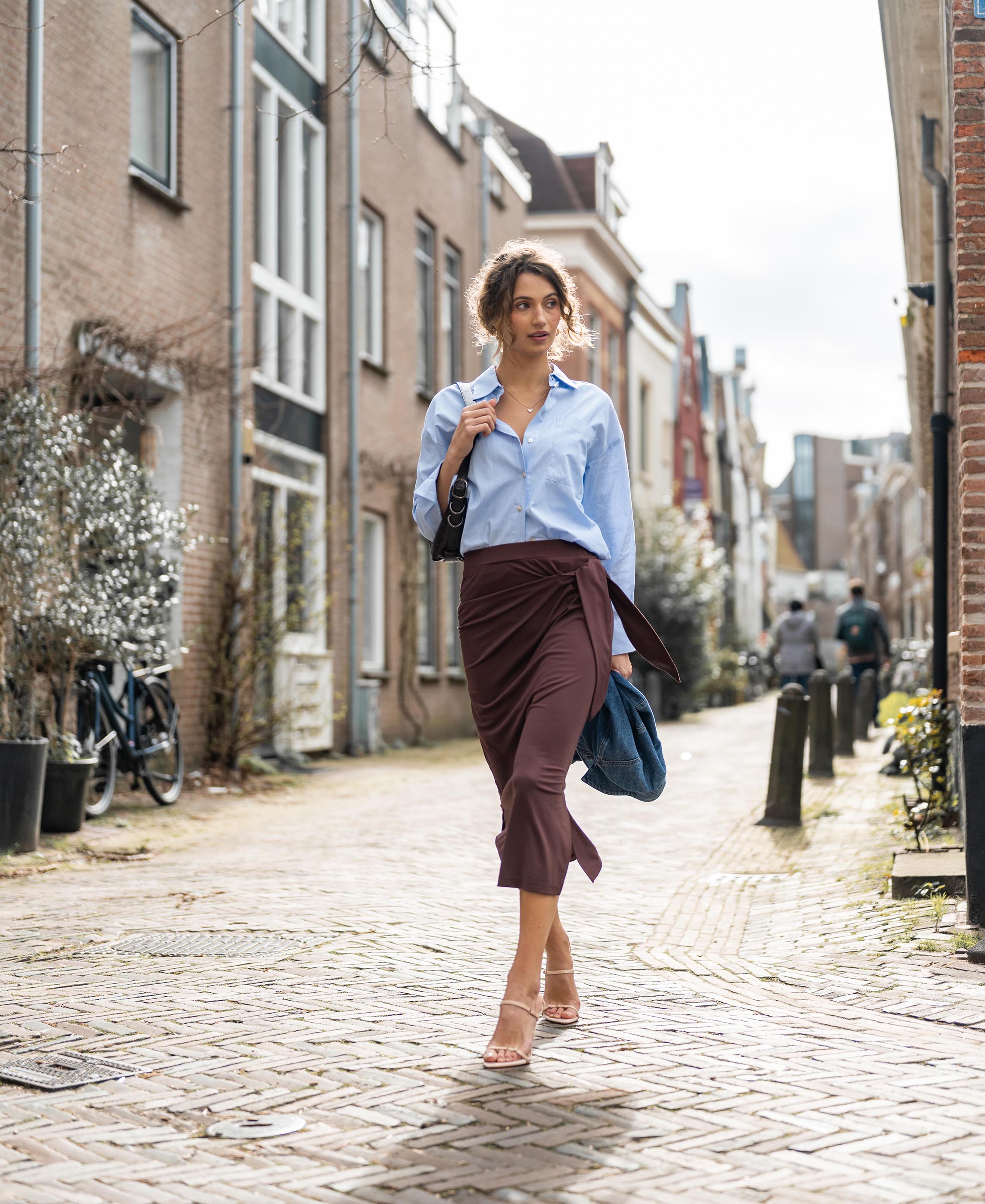 Brown LE MAEL Travel skirt, shown worn by a woman walking on a cobblestone street.