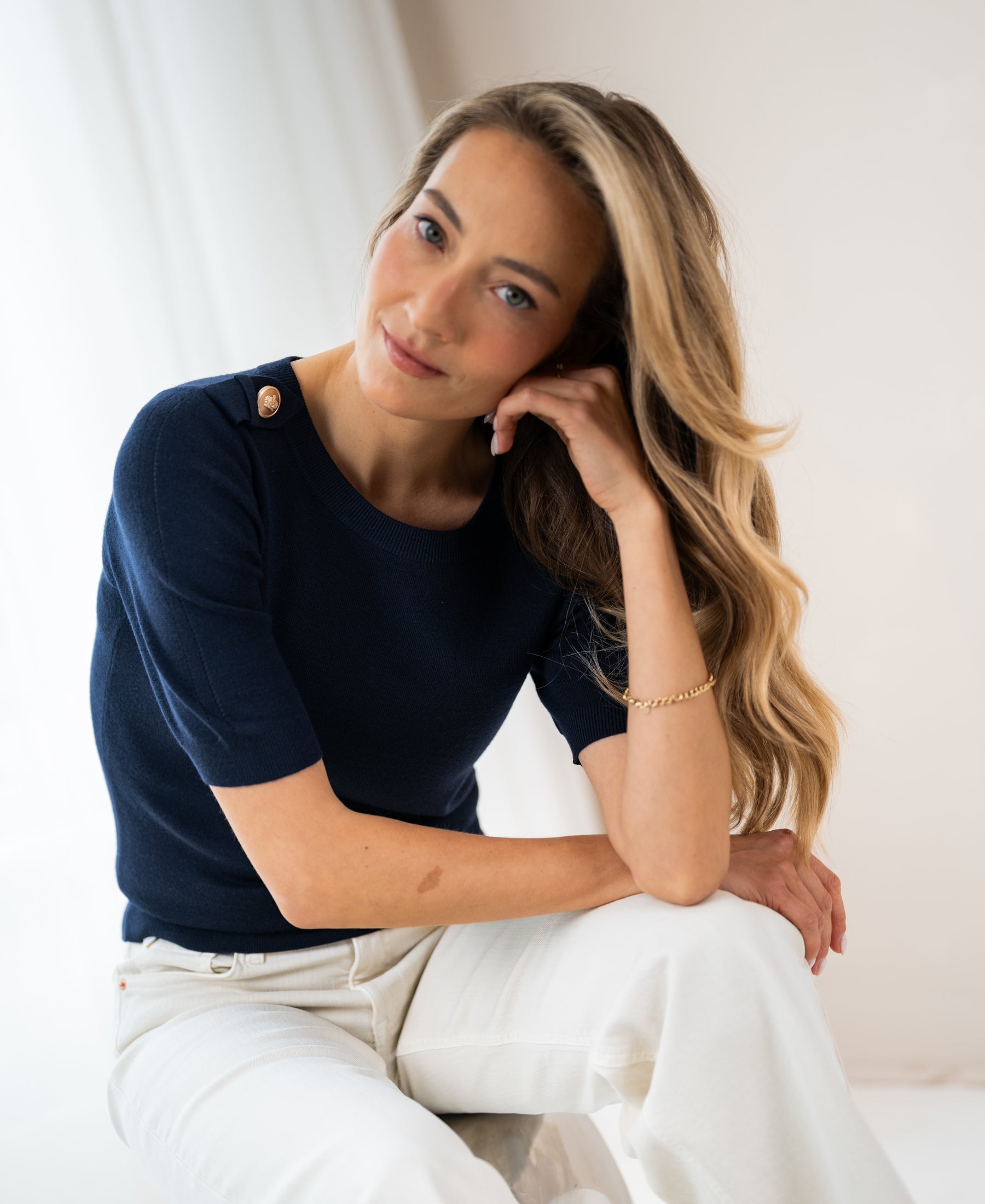 Navy blue Merino wool sweater by PLEIN PUBLIQUE, shown on a woman seated and smiling at the camera.