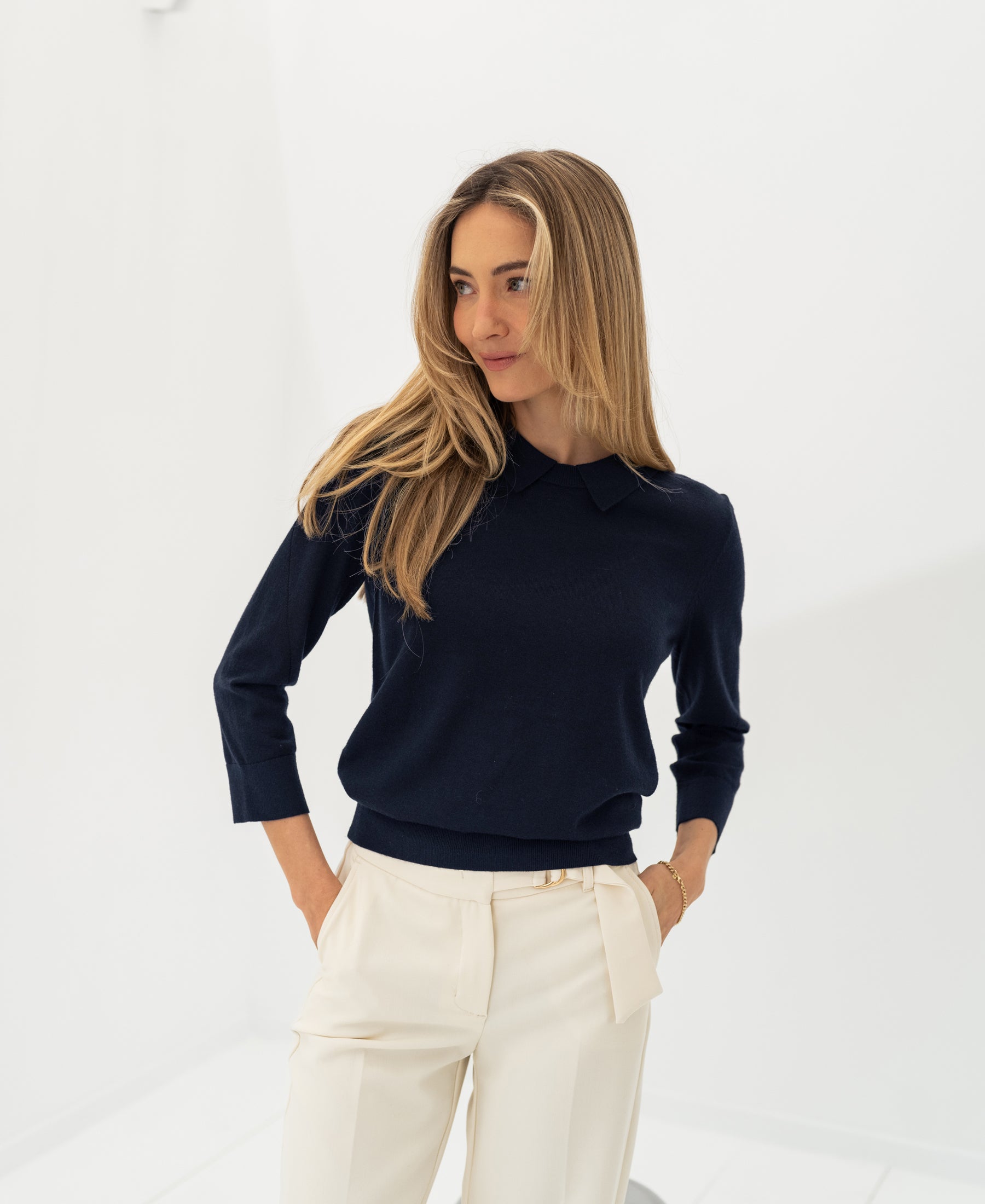 Woman wearing PLEIN PUBLIQUE's dark blue Merino sweater LA MARCEAU in a bright room.
