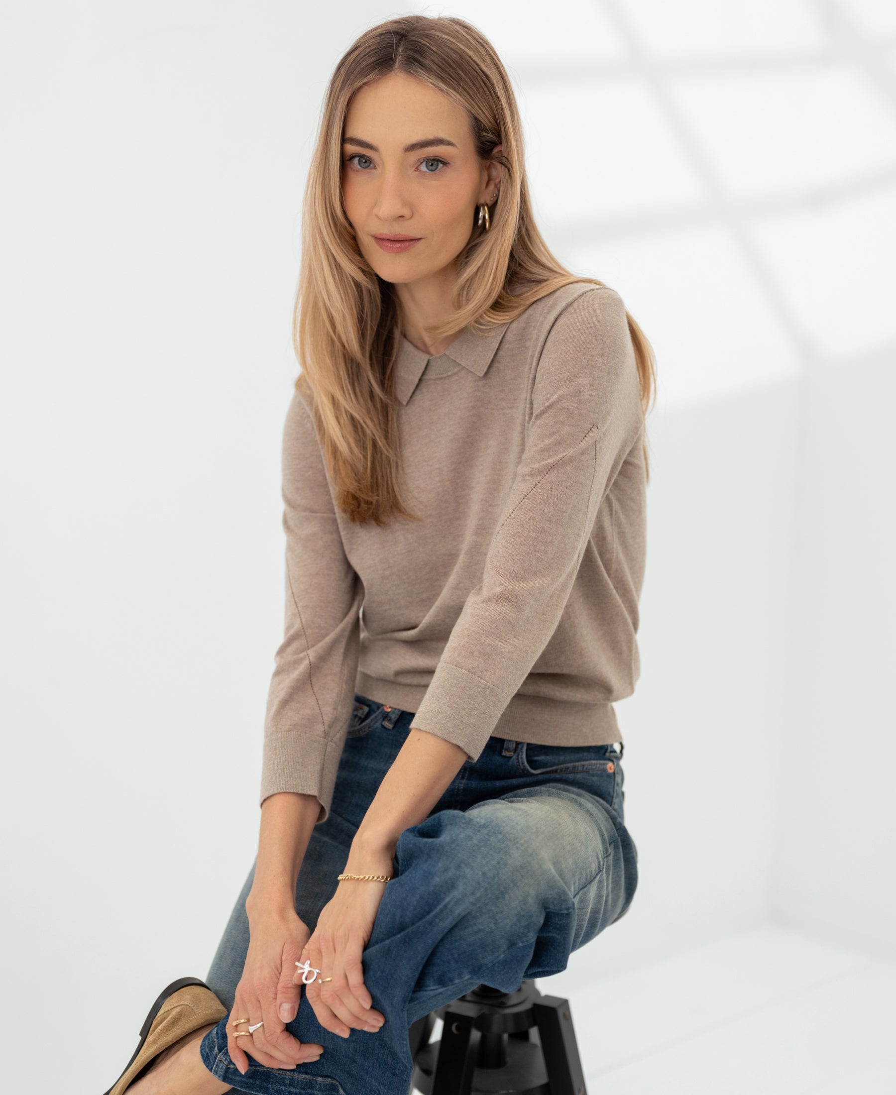 Merino wool polo collar sweater in sand by PLEIN PUBLIQUE, shown in a bright, minimalist room.