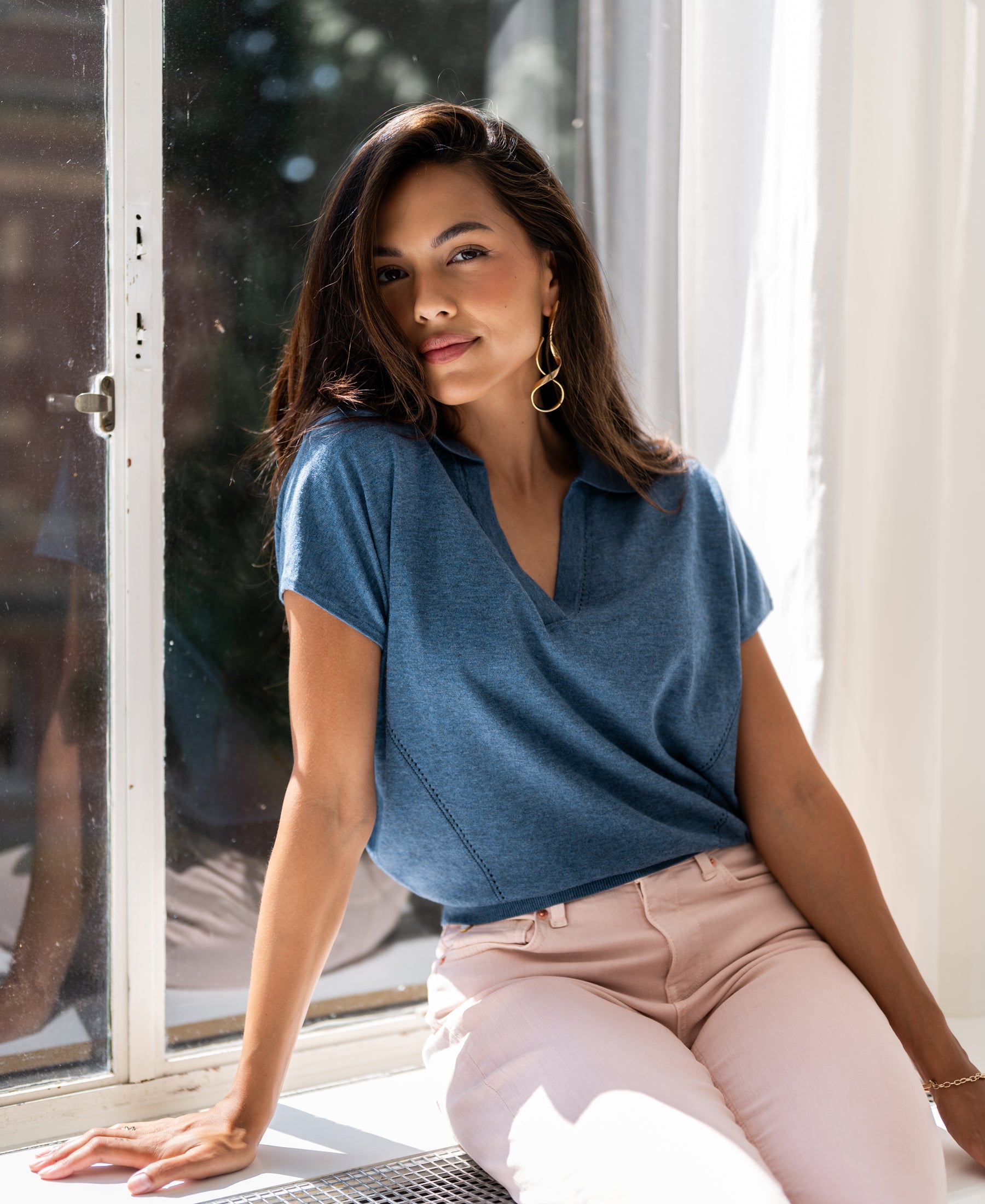 Blue polo-collar sweater by PLEIN PUBLIQUE, product LE MARTIN, shown on a woman sitting by a sunny window.