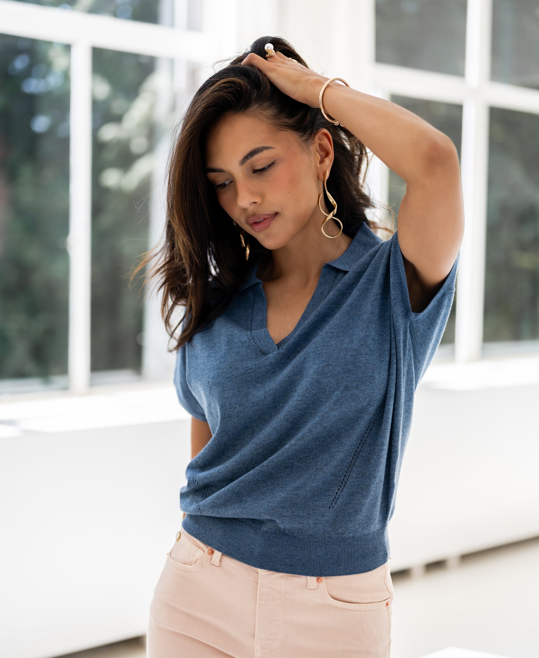 Woman wearing a blue PLEIN PUBLIQUE LE MARTIN polo collar sweater indoors, soft light in the background.