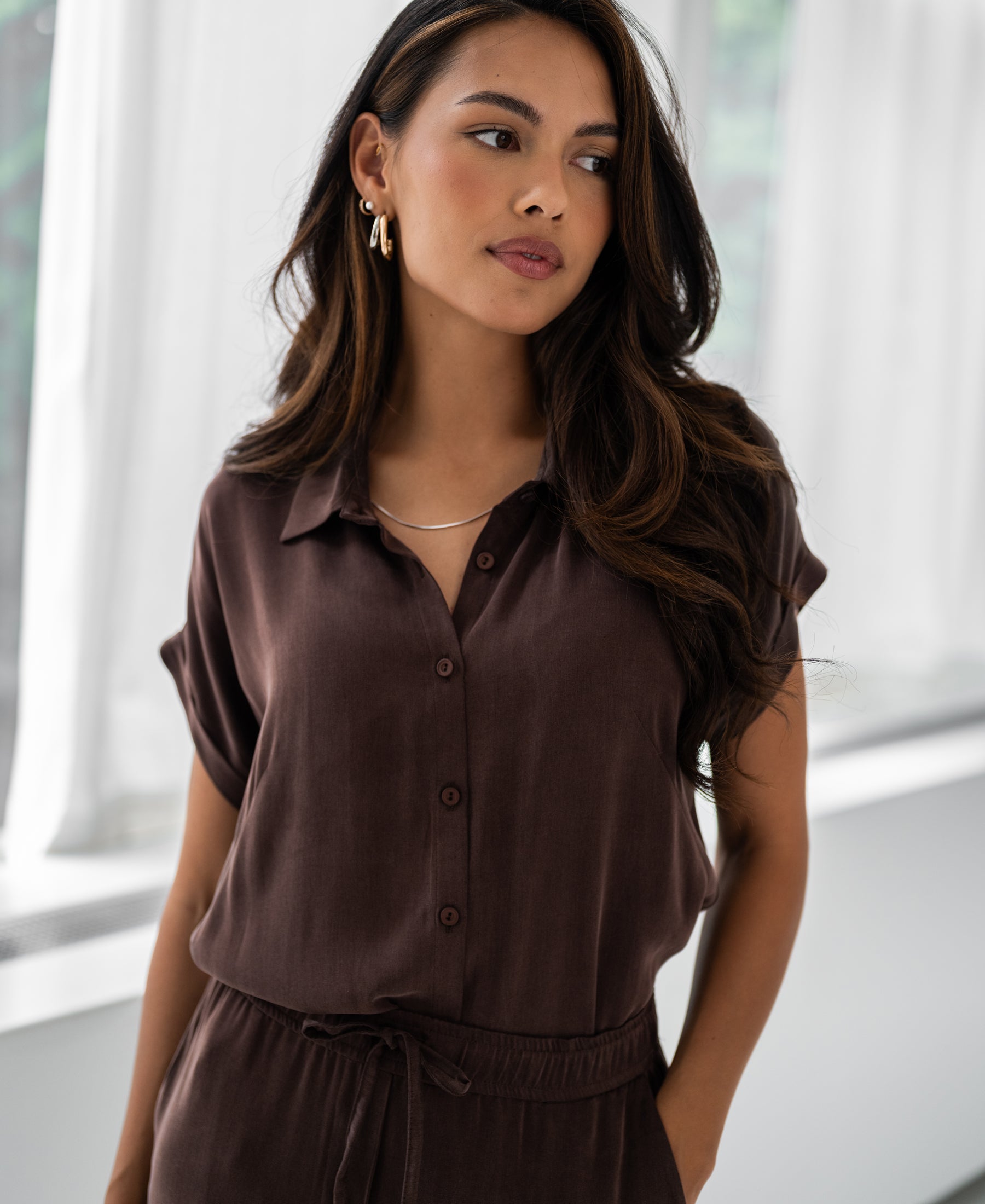 Cupro blouse in cacao brown from PLEIN PUBLIQUE, shown indoors near white curtains.