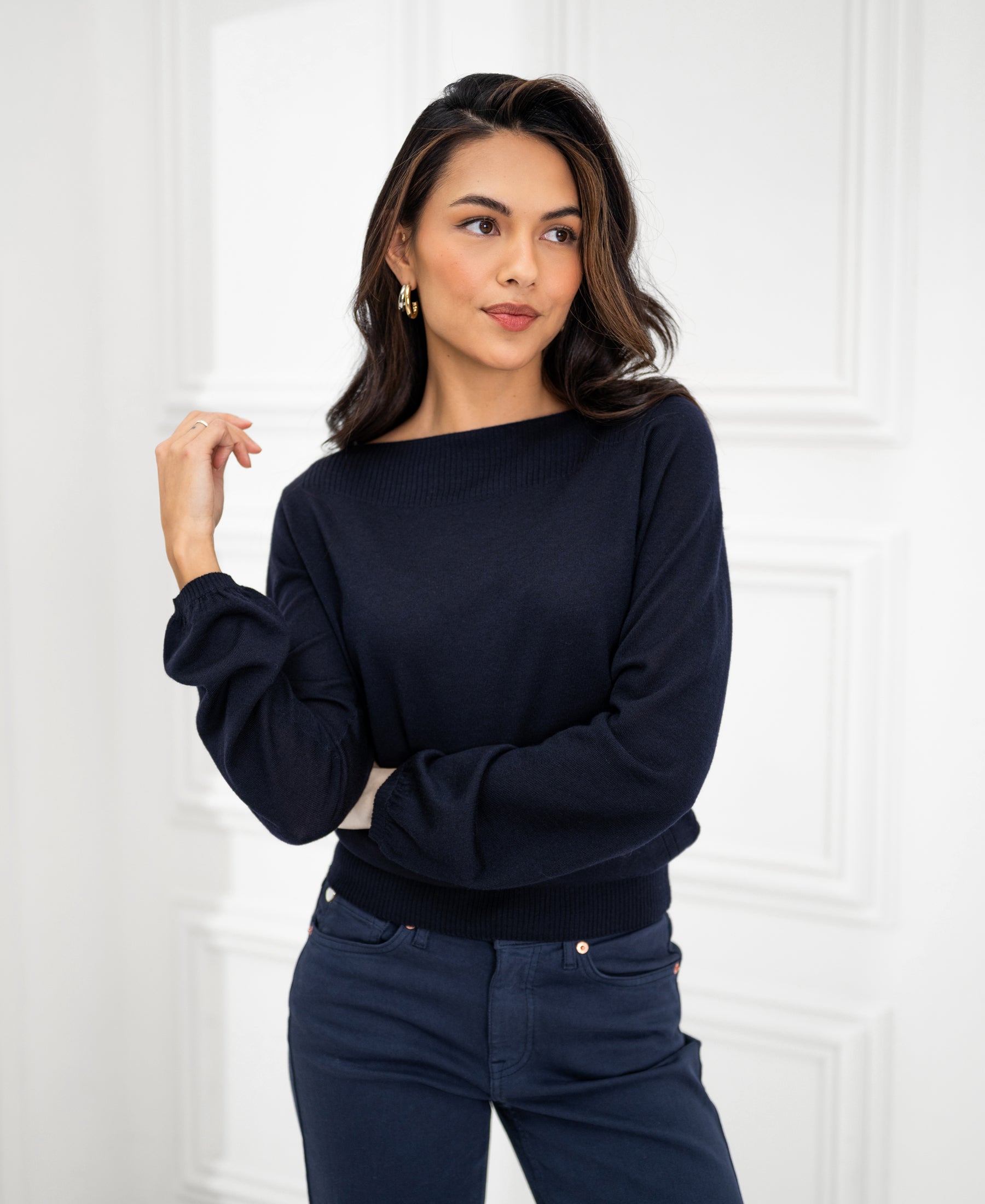 Navy blue boat neck sweater from PLEIN PUBLIQUE displayed on a person standing by a white paneled wall.