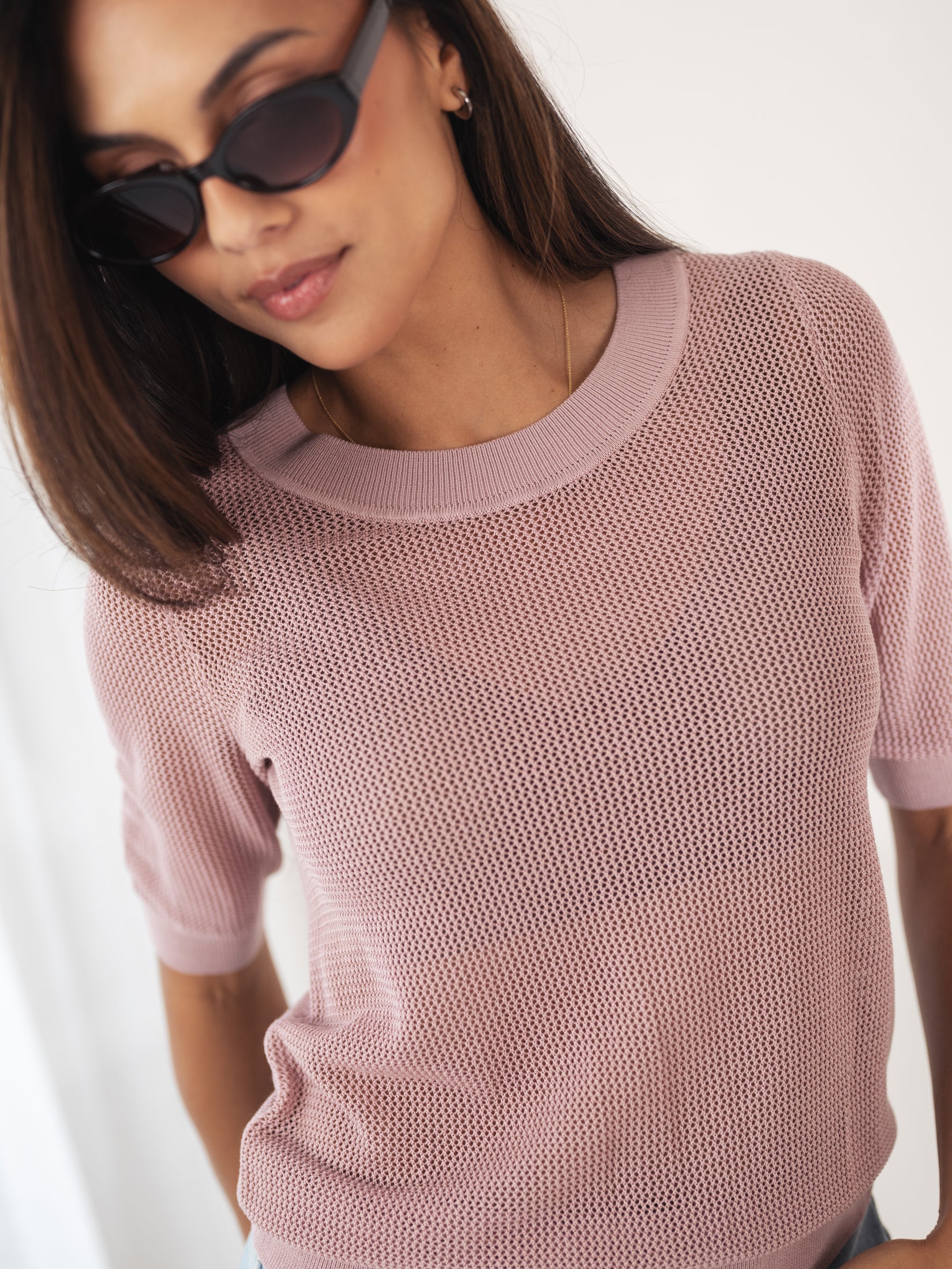 Woman wearing dusty pink mesh sweater with silk, straight brown hair visible, looking down.