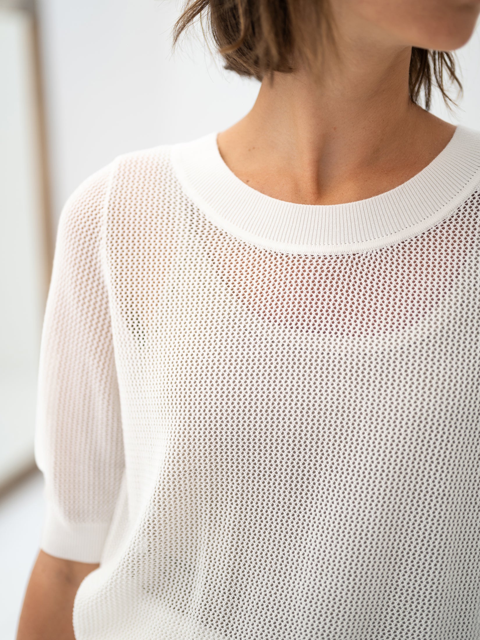 The white mesh sweater with silk by PLEIN PUBLIQUE, shown on the lower face, neck, and torso of a woman.