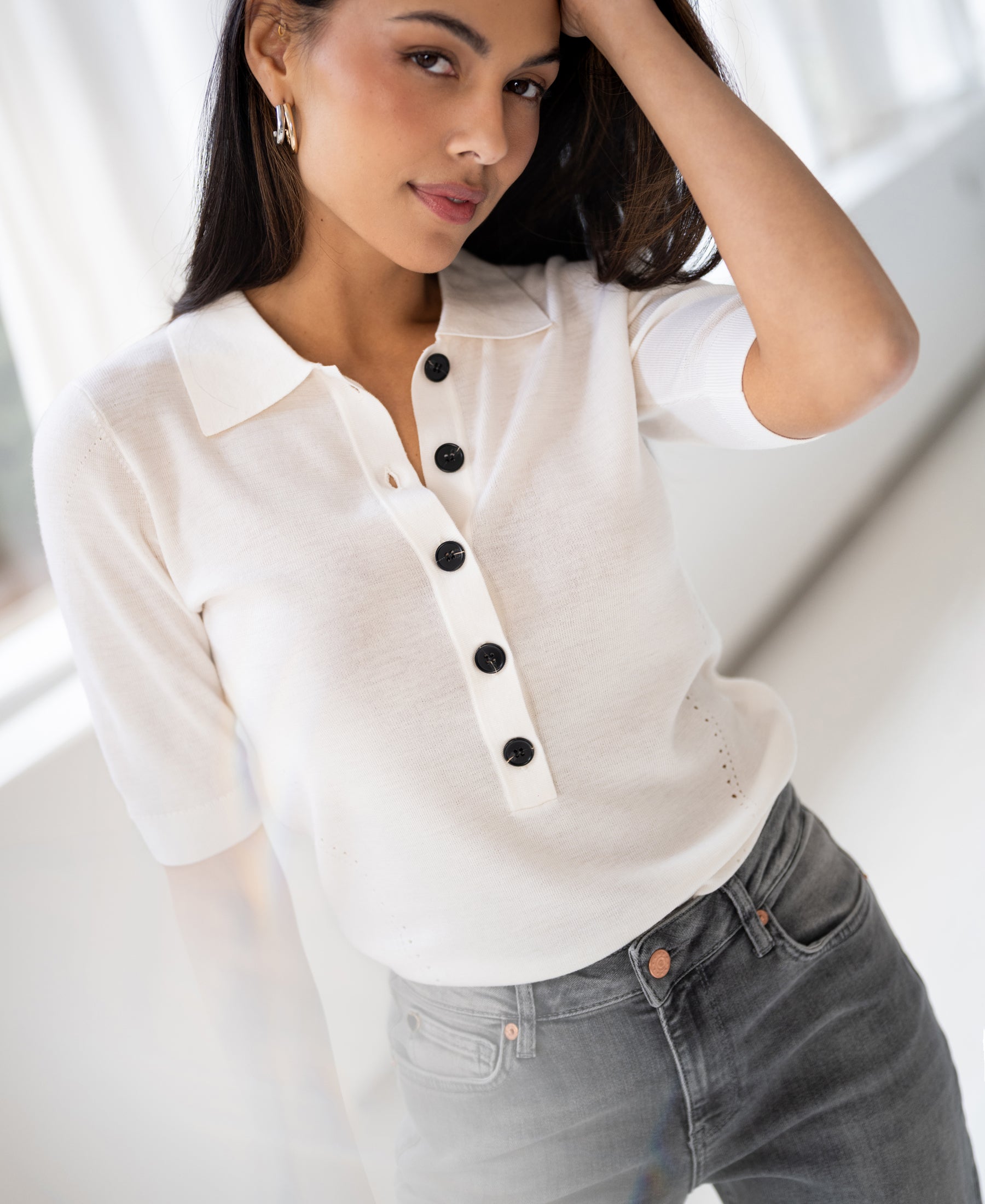 Woman wearing an ivory Merino wool polo sweater by PLEIN PUBLIQUE, posing indoors and looking at the camera.