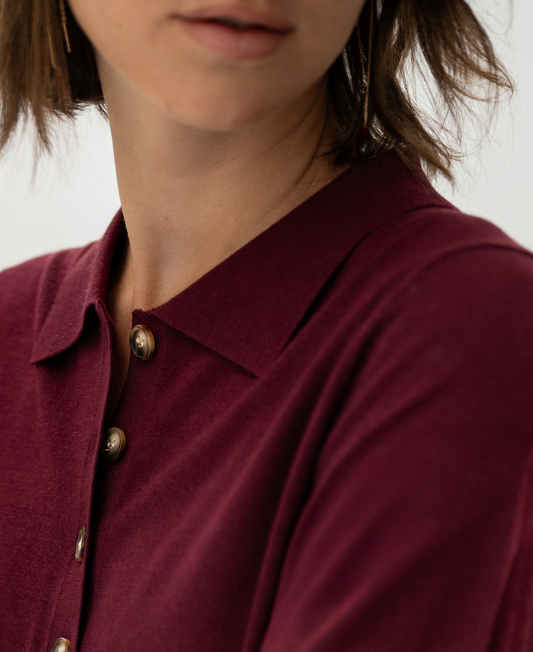 Close-up of a woman wearing a plum Merino silk polo shirt, showing only her lower face and upper torso.
