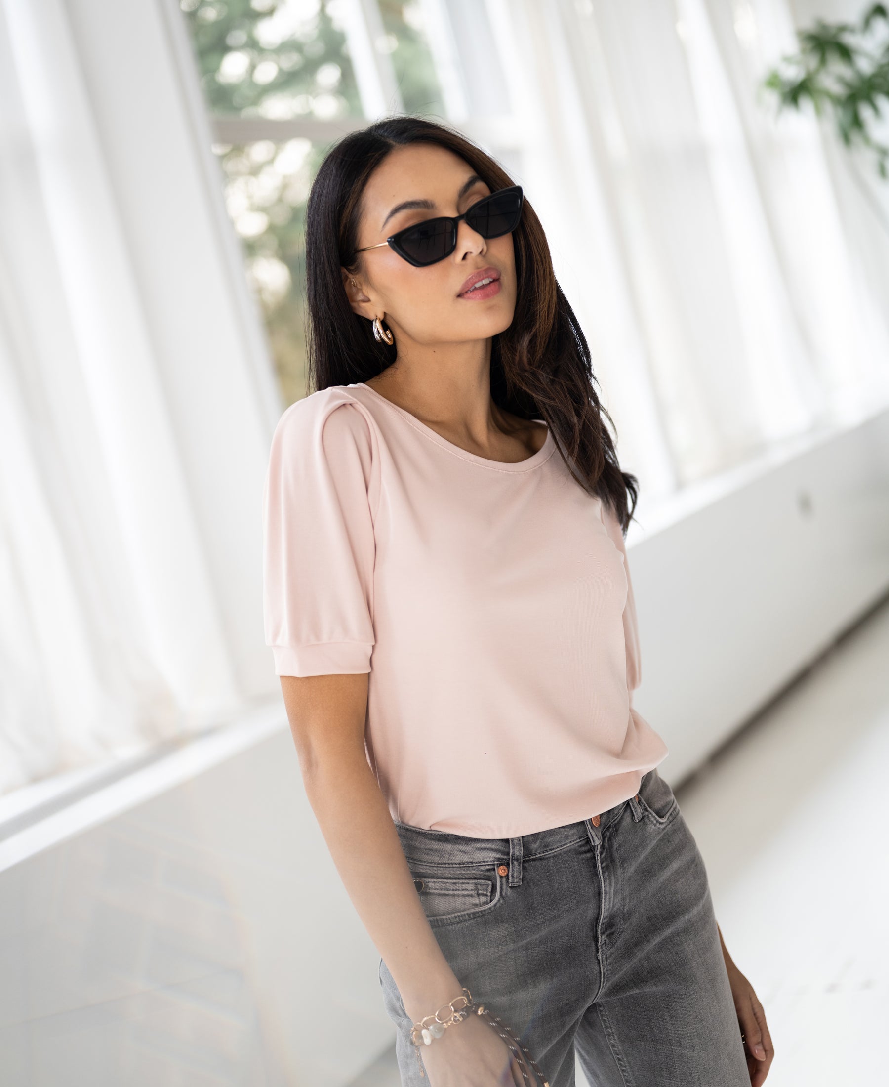 Woman wears a blush ribbed T-shirt in a bright room with large windows.