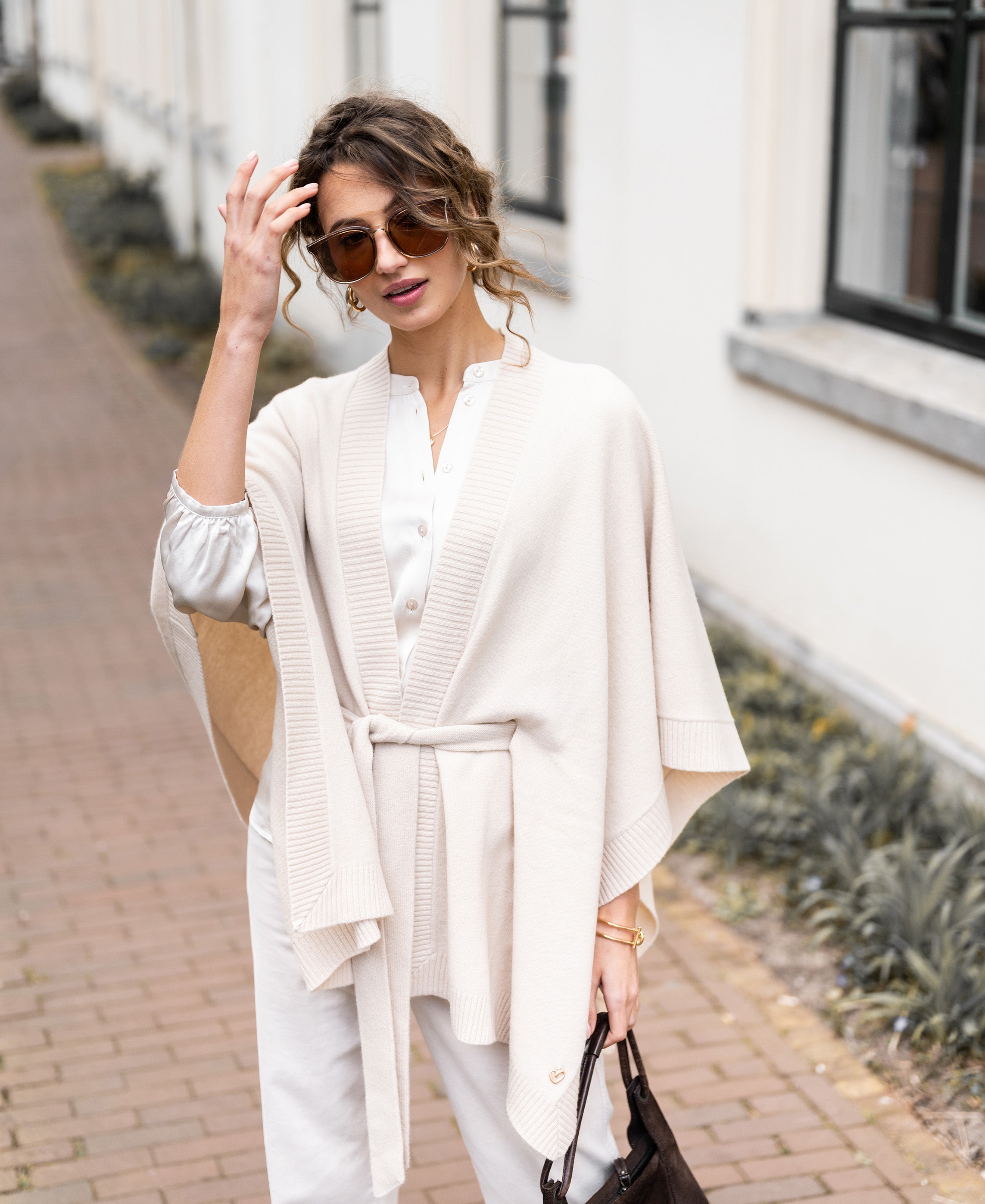 Woman wearing a light sand merino wool poncho stands on a brick sidewalk.