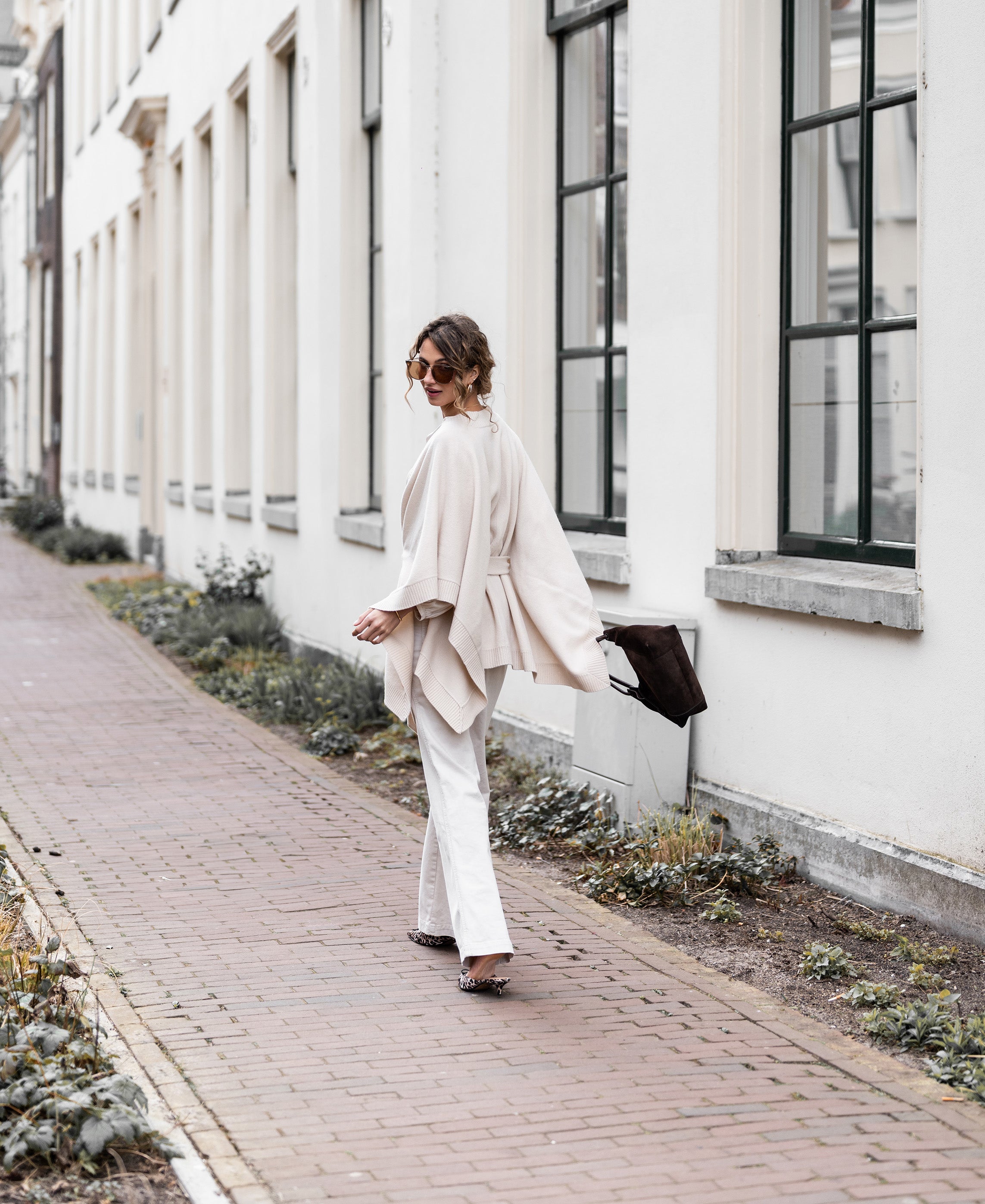 Light sand merino wool poncho by PLEIN PUBLIQUE, shown on model walking outside.