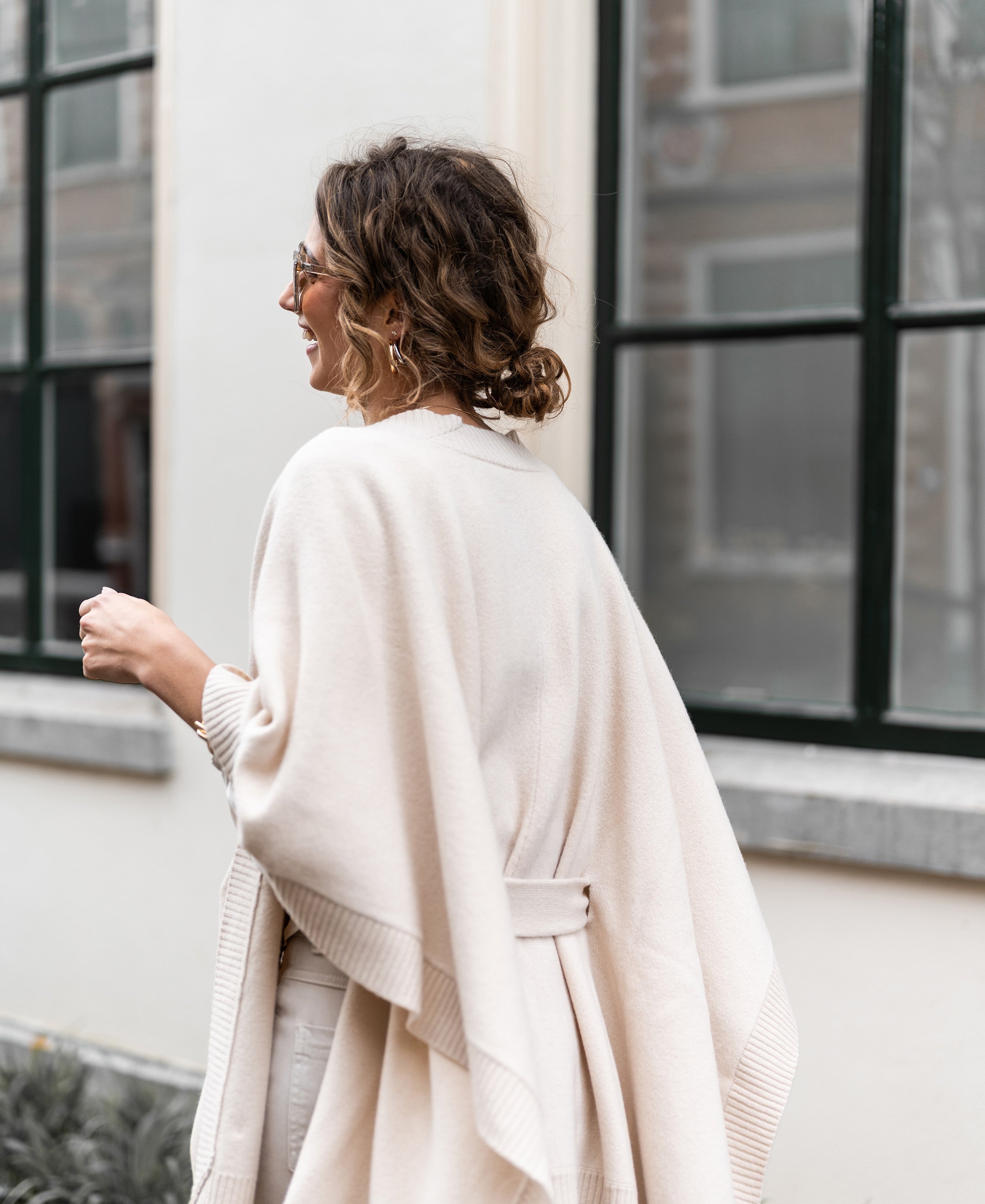 Light sand-colored merino wool poncho displayed by large windows.