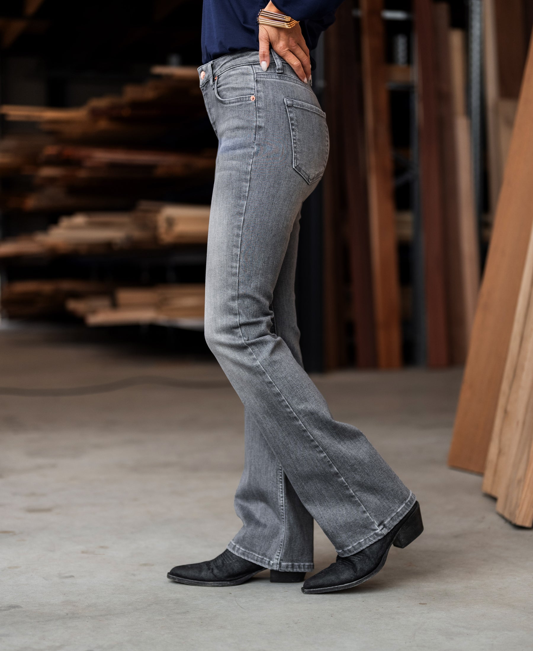 Grey stonewash flared jeans, shown indoors near stacked wooden boards.