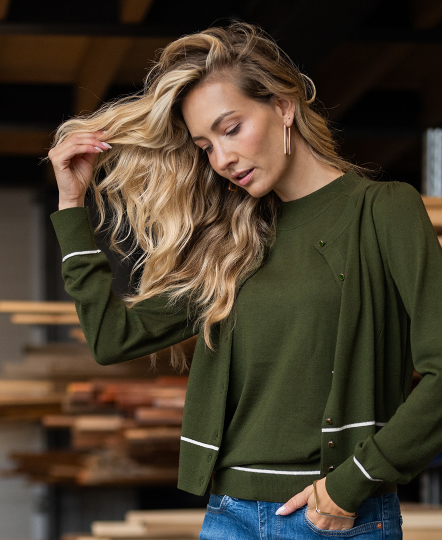 Woman wearing SALE LA SARA Army-Ivory Cardigan, standing indoors near stacked wood.