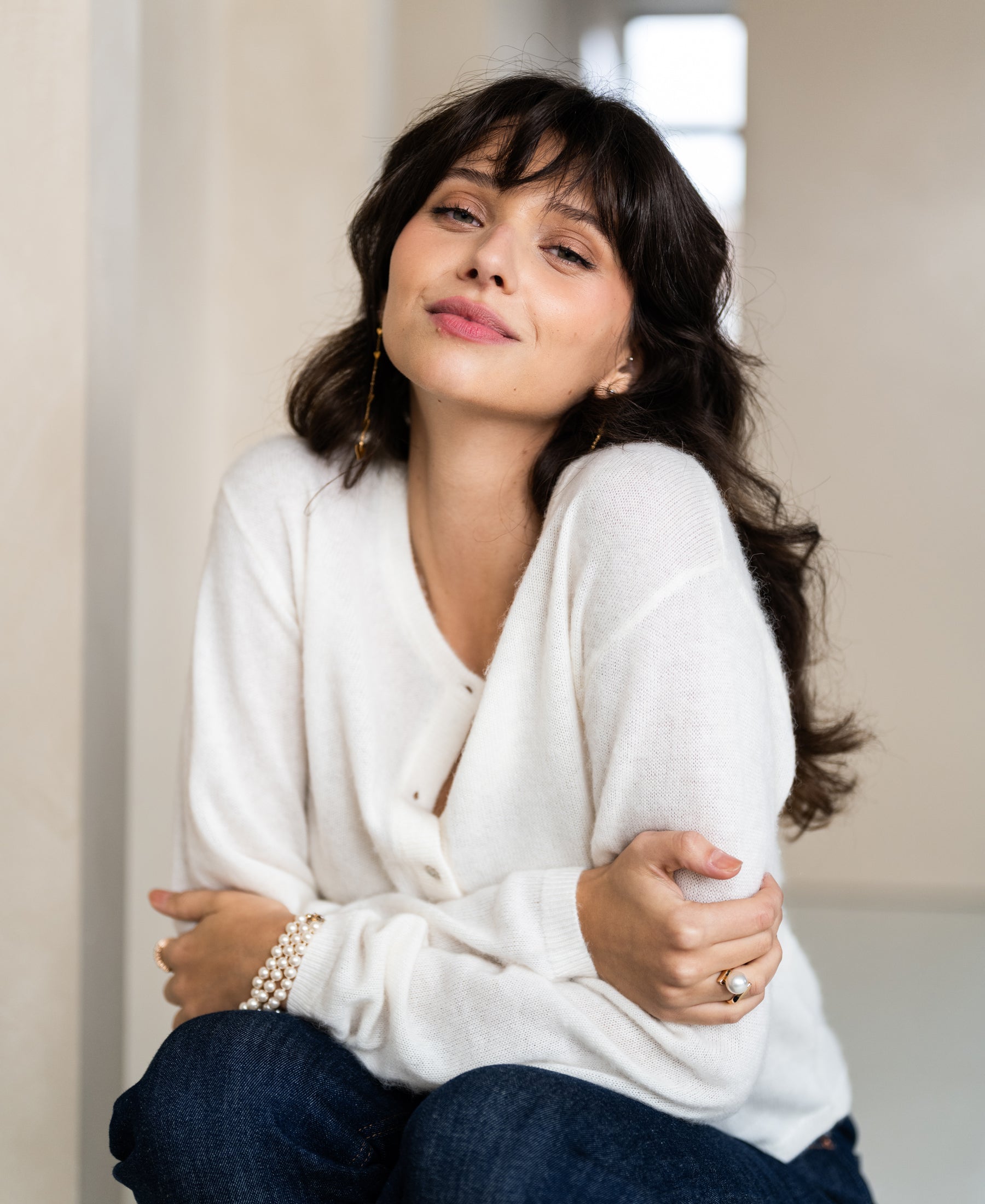 Woman wearing sale wool vest La Quarte in ivory, sitting and smiling gently with arms crossed.