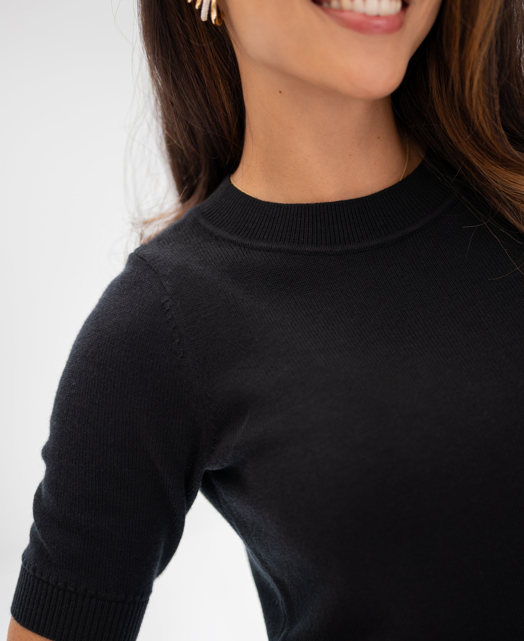 Black cotton-merino wool sweater, front view, on woman with long brown hair against a white background.