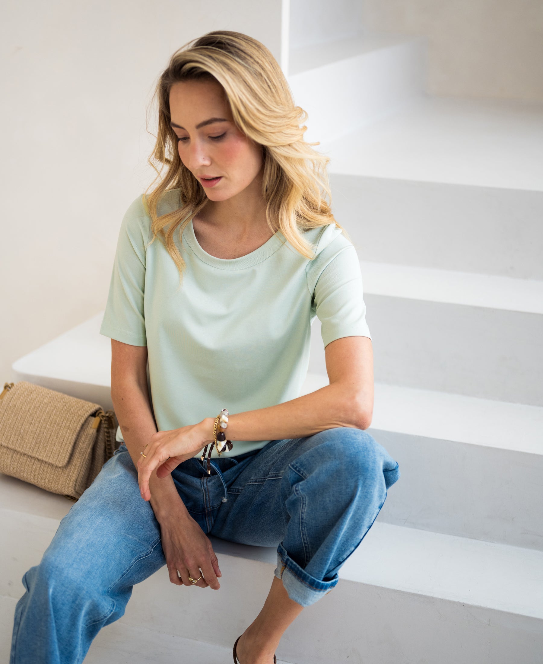 Light green stretch T-shirt with short sleeves by PLEIN PUBLIQUE, shown worn by a model sitting on white stairs.