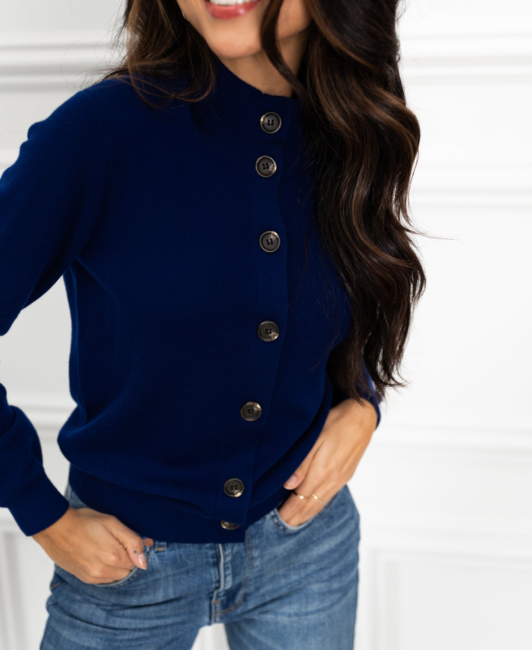 Smiling woman wearing the LES SEIZE Navy Merino turtleneck cardigan, hands in pockets.