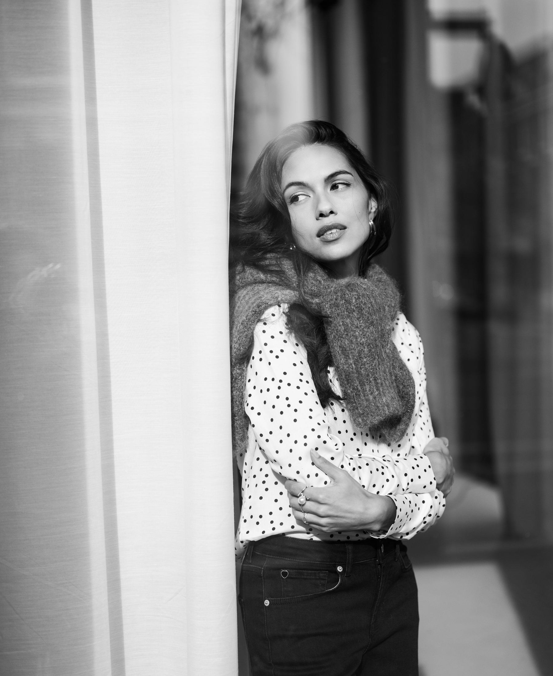 Ivory-black polka dot blouse by PLEIN PUBLIQUE, shown on a woman leaning against a wall, side view.