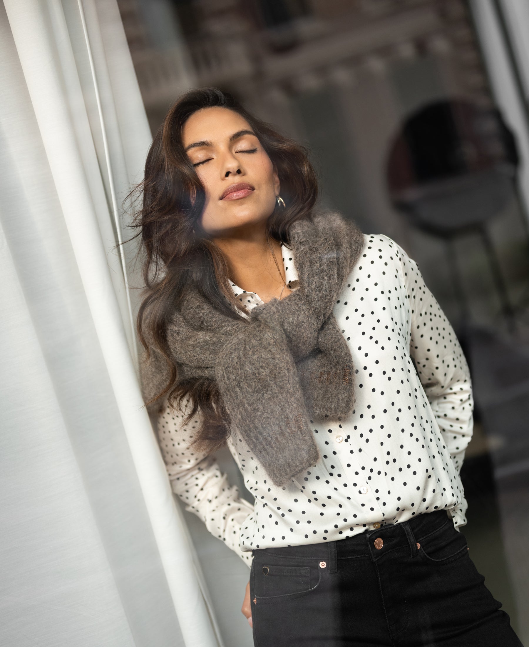 Ivory-black polka dot blouse by PLEIN PUBLIQUE, shown on a woman standing by a window.