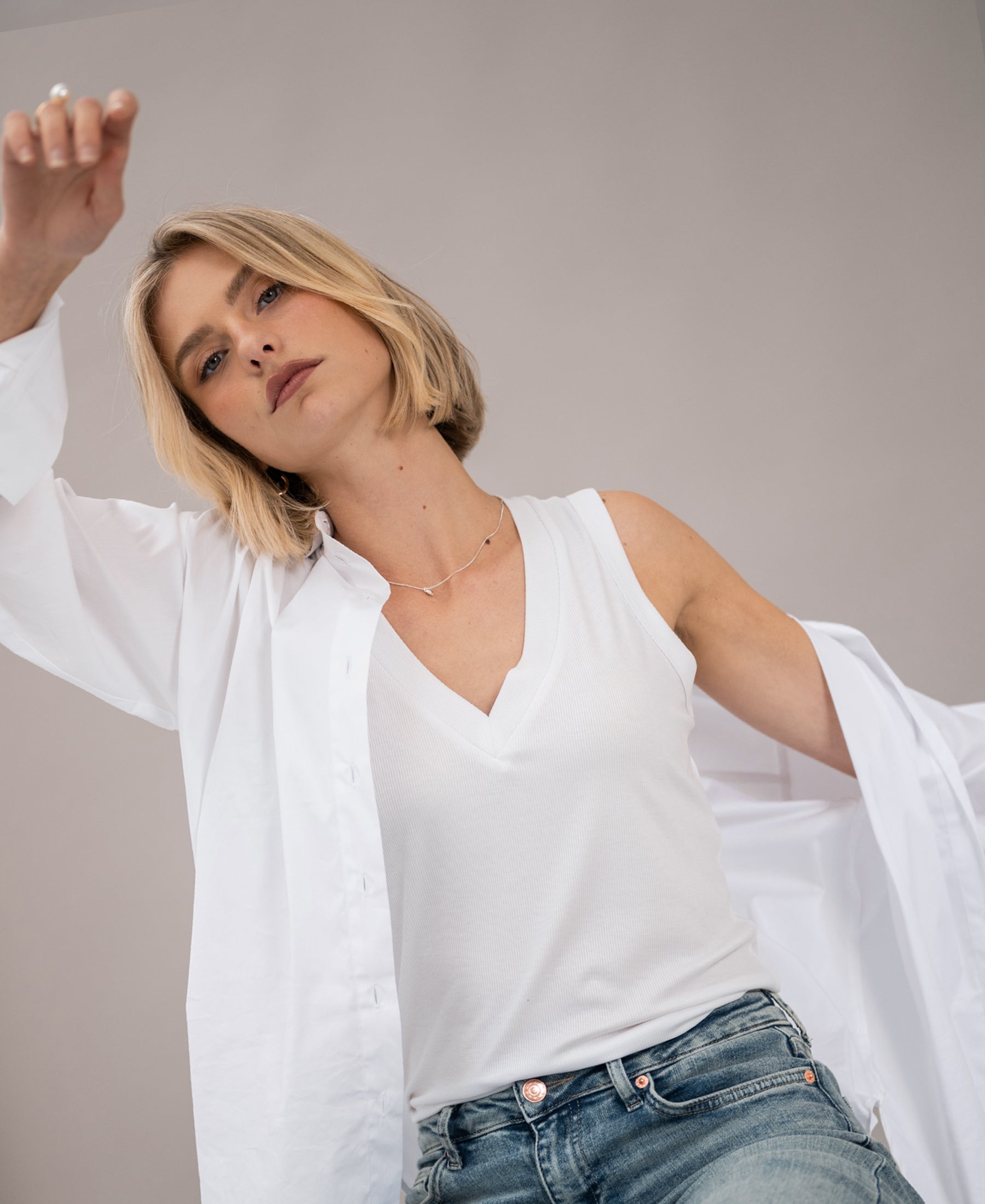 Woman wears a white lyocell top, posing with one arm raised.