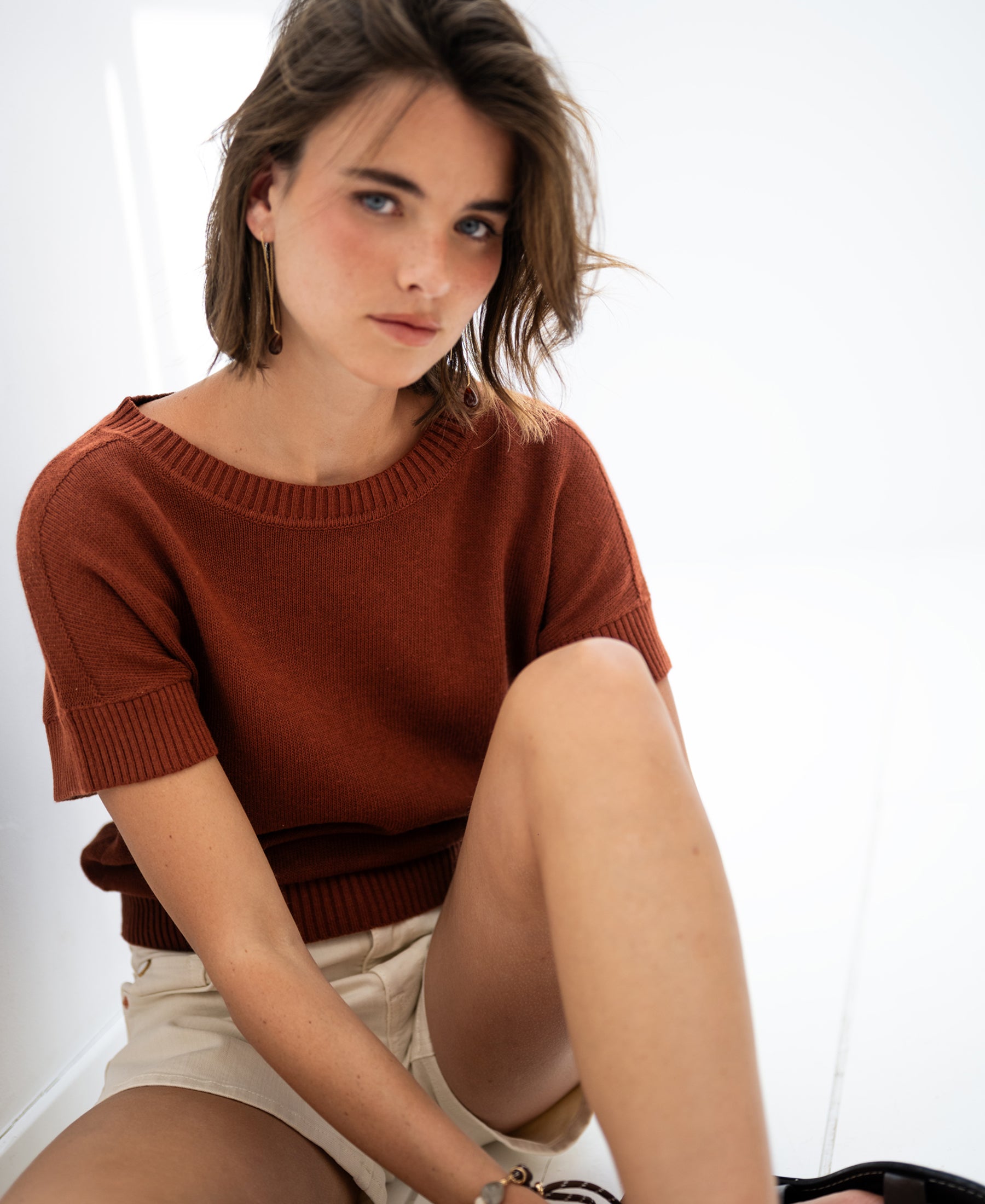 Linen summer sweater in Sierra color, shown worn by a woman sitting on a white floor.