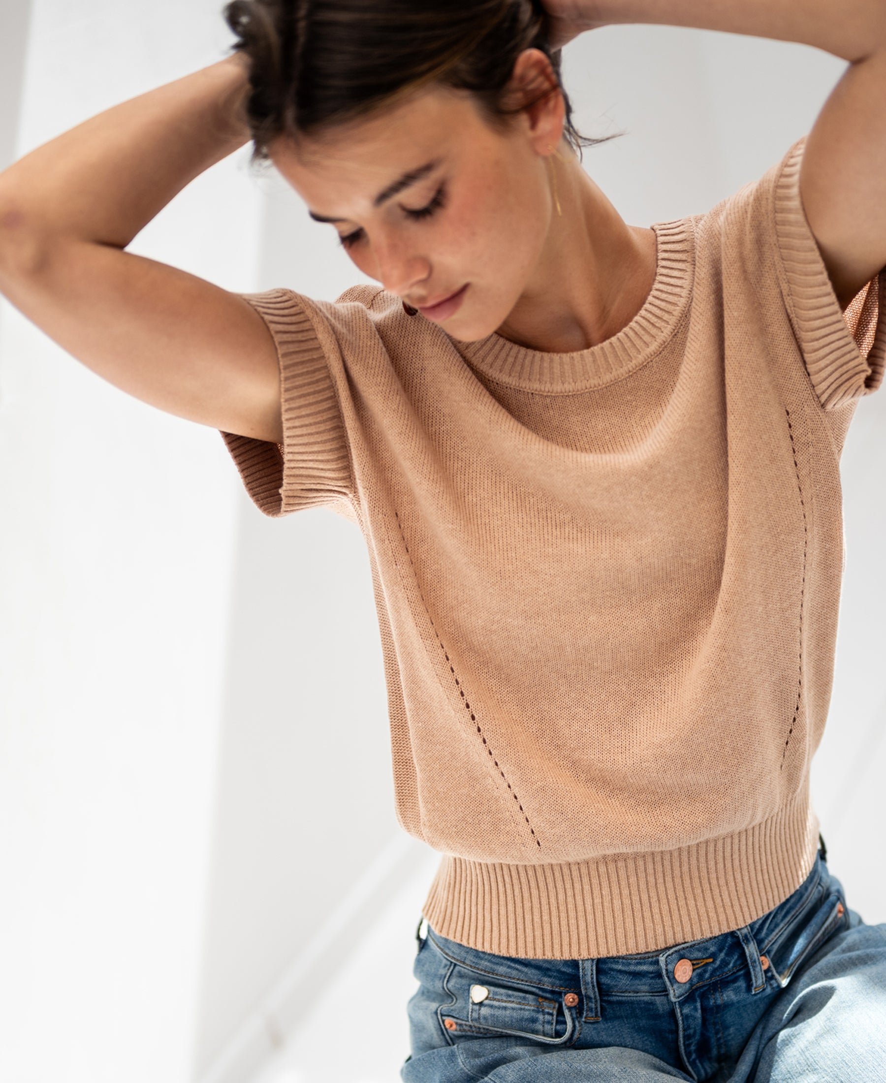Woman wearing the LE SOLEIL soft camel linen summer sweater, standing with arms raised in natural light.