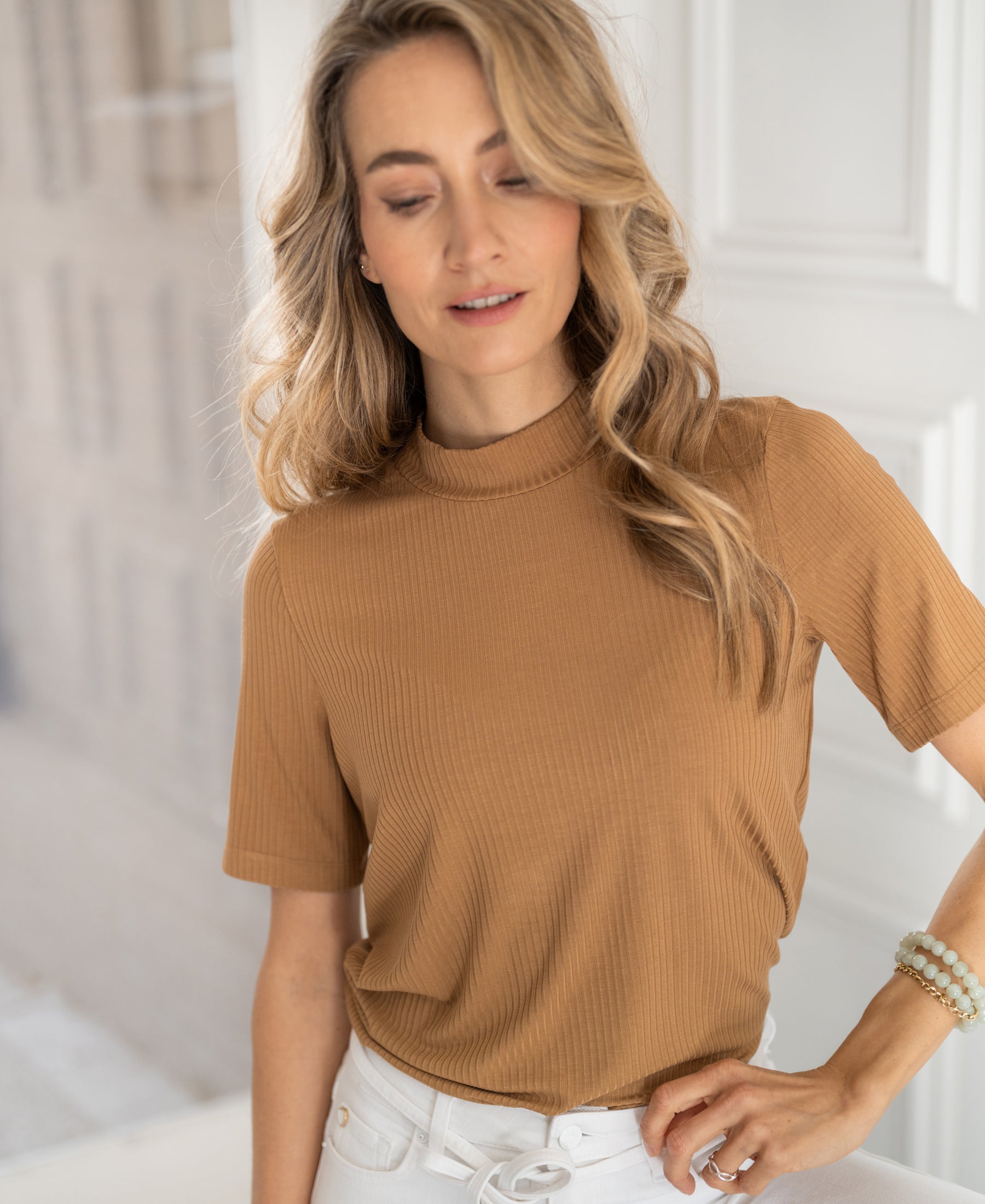Woman wearing a gold-yellow bamboo turtleneck top, standing indoors.
