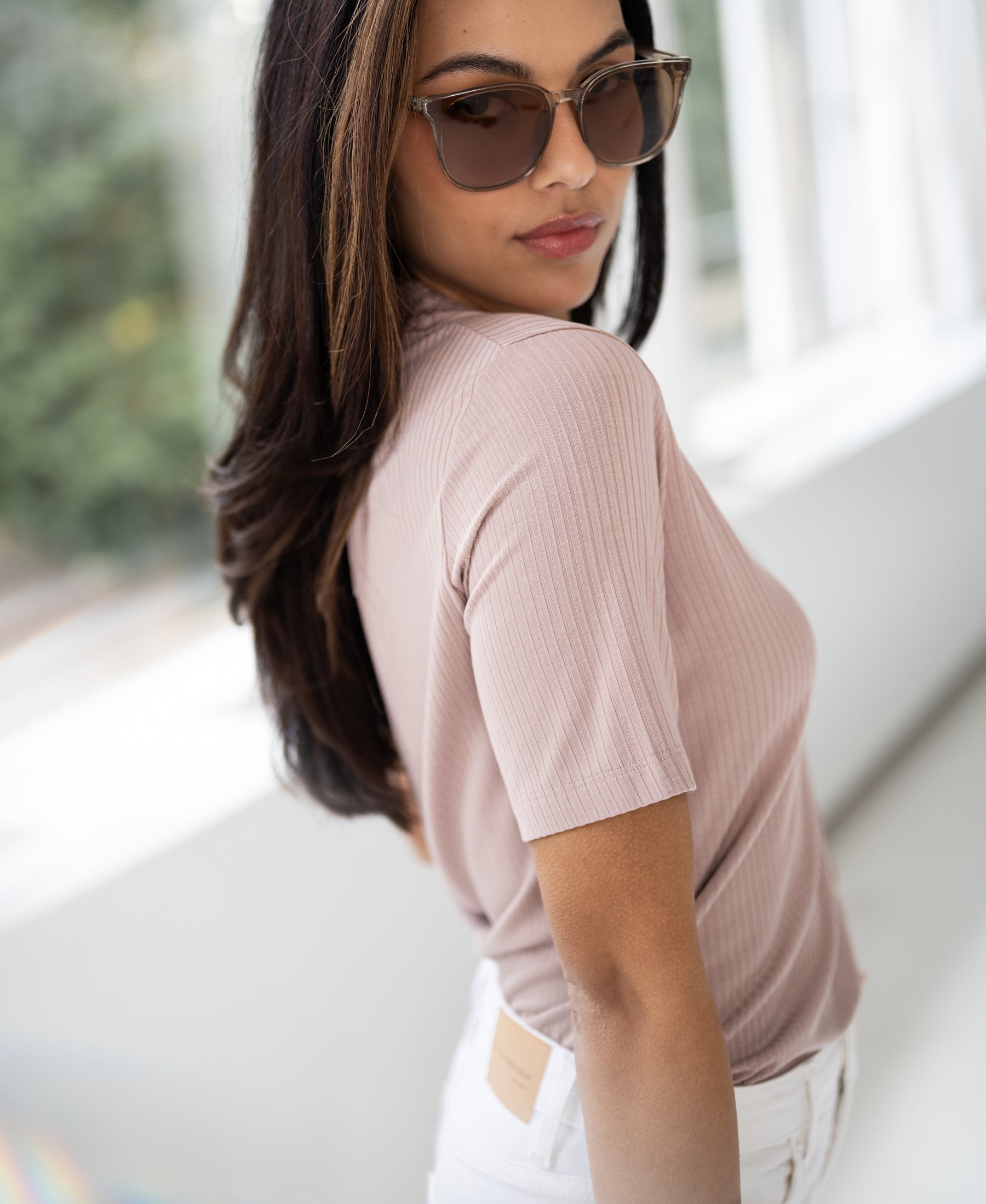 Woman wearing a dusty pink bamboo turtleneck top stands by a window.